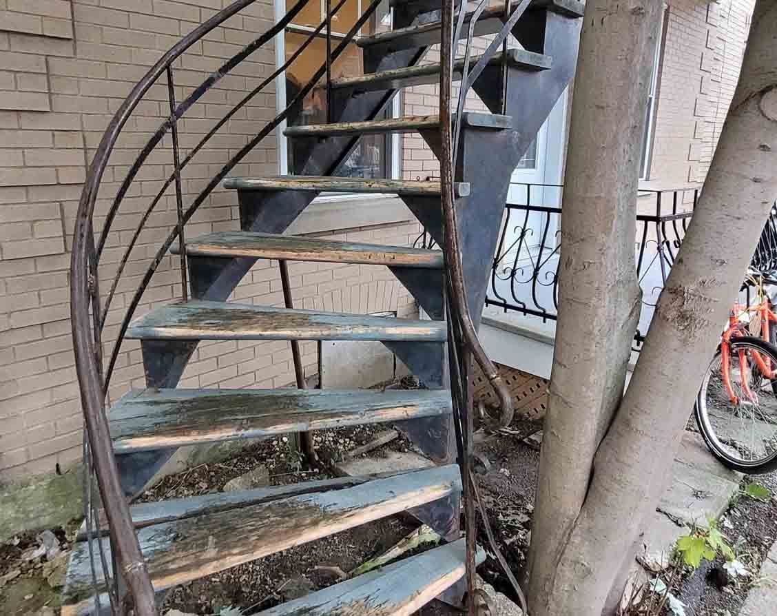 Escalier en colimaçon extérieur rouillé, adossé à un mur de briques, avec un vélo en arrière-plan.