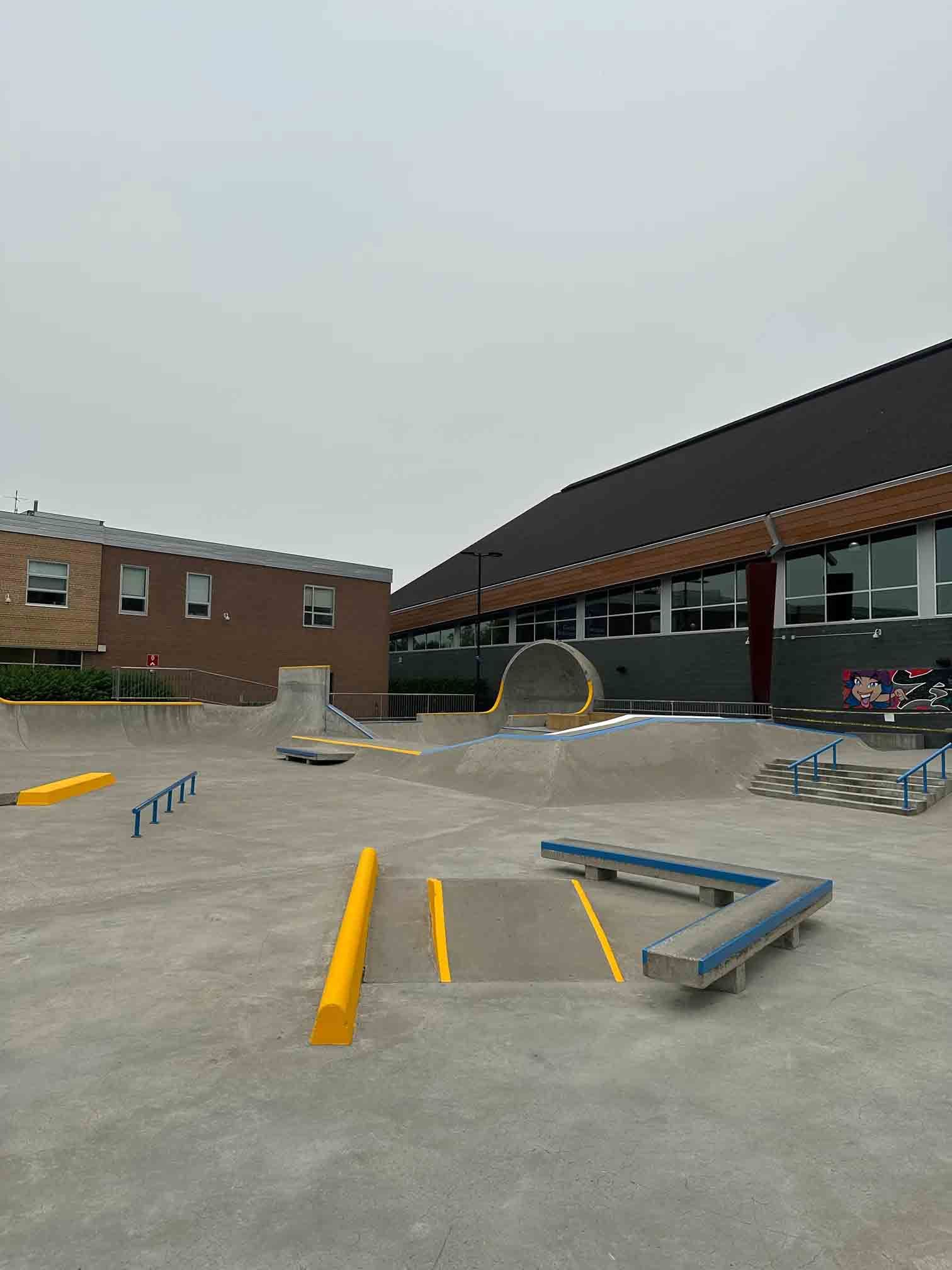 Skatepark de cour d'école avec rampes, rails et obstacles en béton à côté de bâtiments en briques