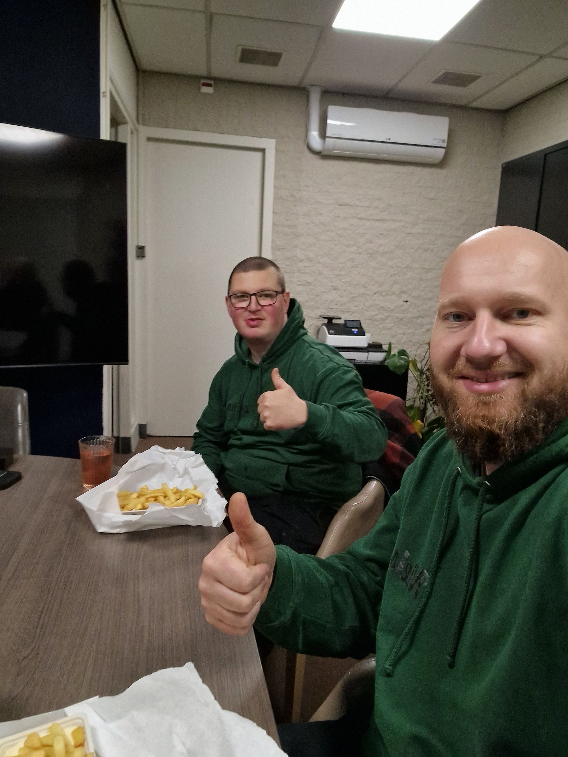 Twee mannen zitten aan een tafel met frietjes en steken hun duim omhoog. Dagbesteding Samen102