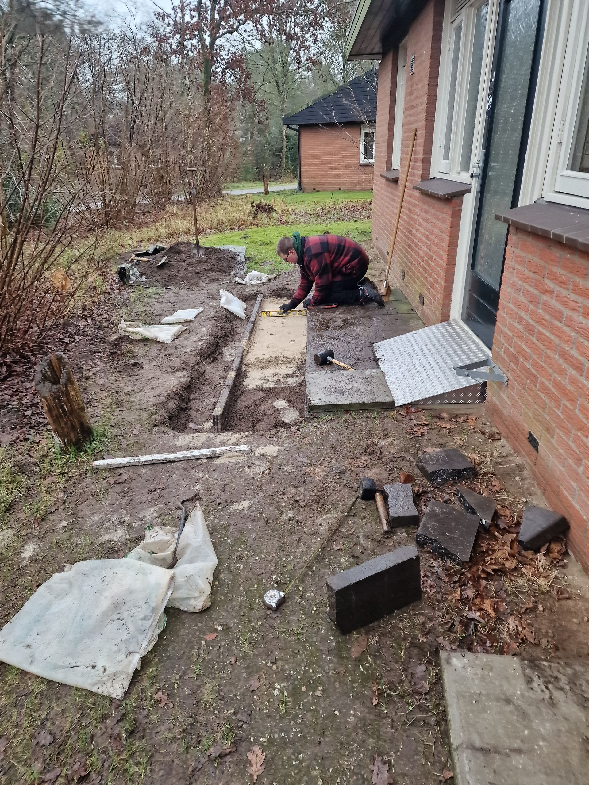 Een man knielt op de grond voor een bakstenen gebouw. Dagbesteding Samen102