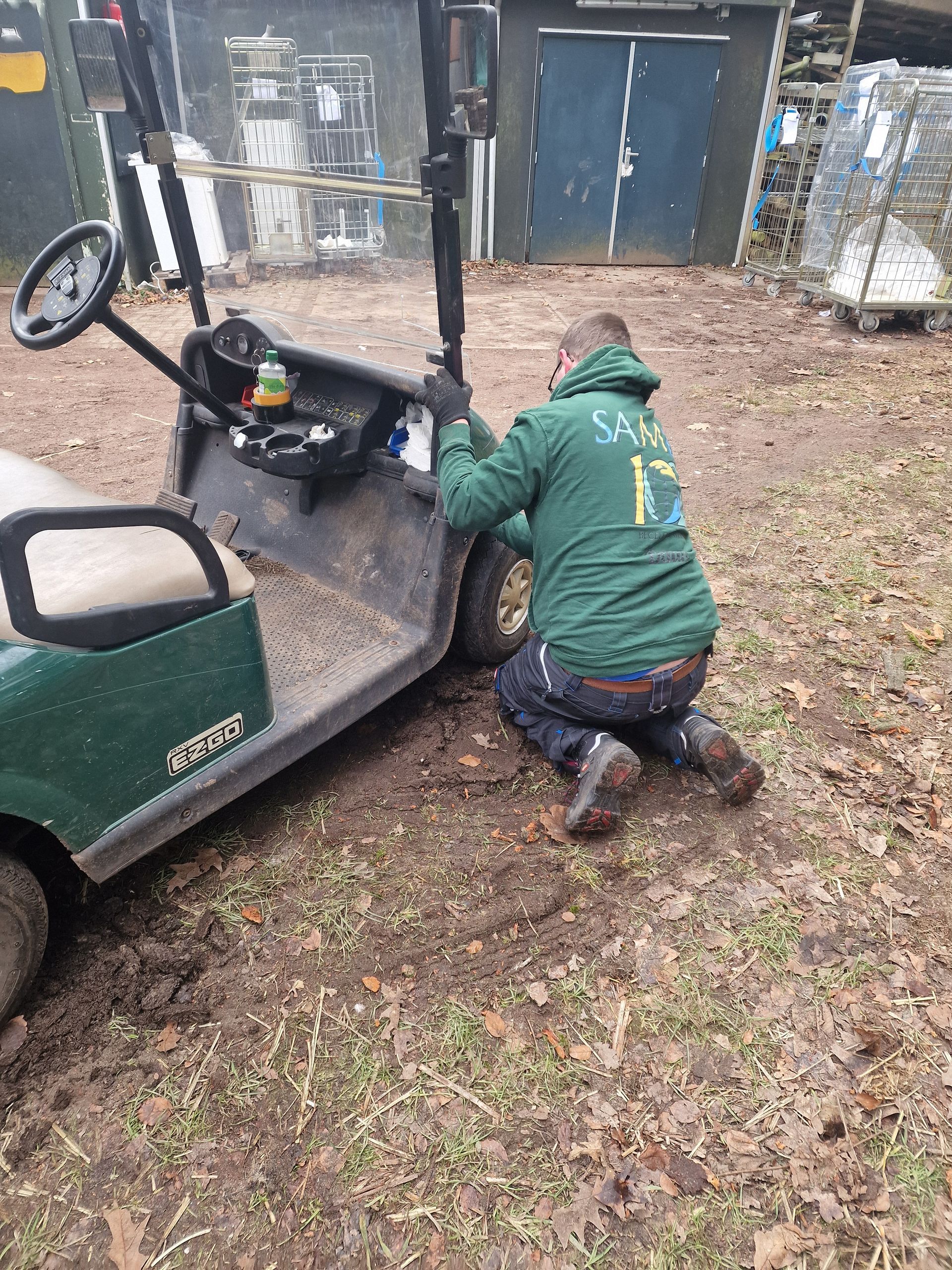 Een man knielt naast een golfkarretje. Dagbesteding Samen102