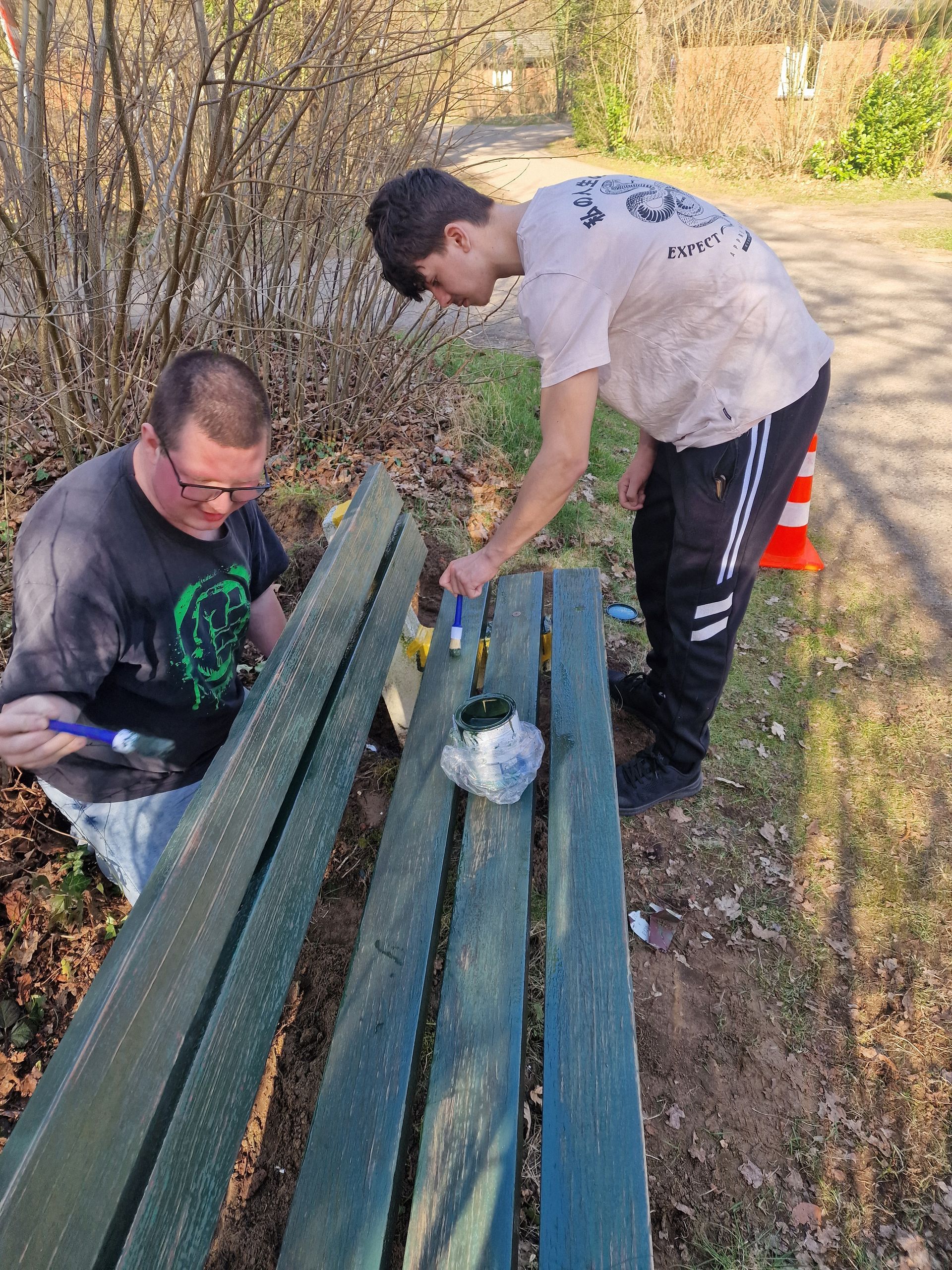 Twee mannen schilderen een houten bank in een park. Dagbesteding Samen102