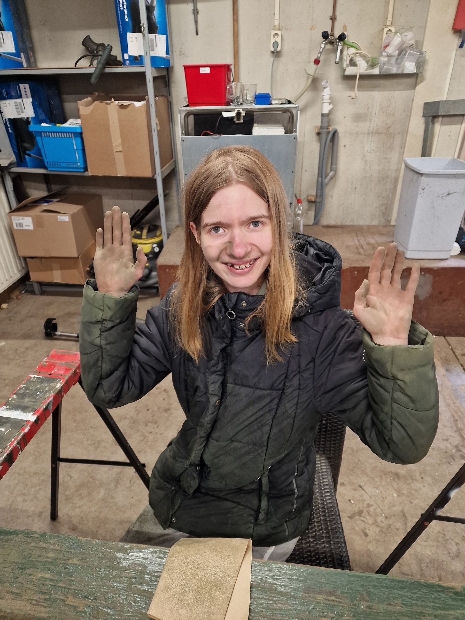 Een vrouw zit aan een tafel met haar handen in de lucht. Dagbesteding Samen102