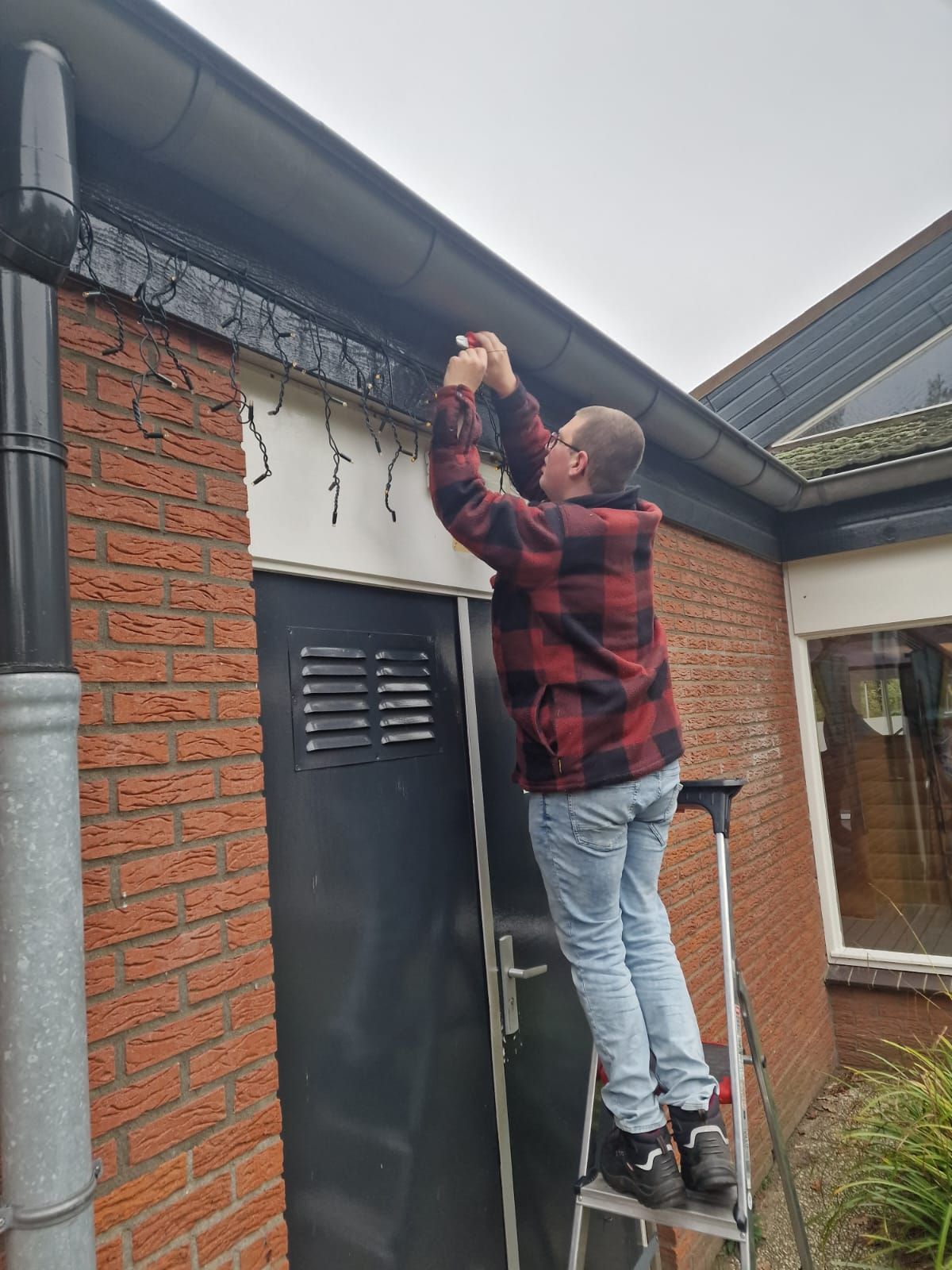 Een man staat op een ladder en bevestigt een lamp aan de zijkant van een bakstenen gebouw.
