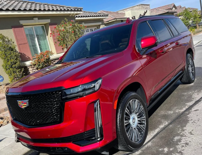 A red cadillac escalade is parked on the side of the road in front of a house.