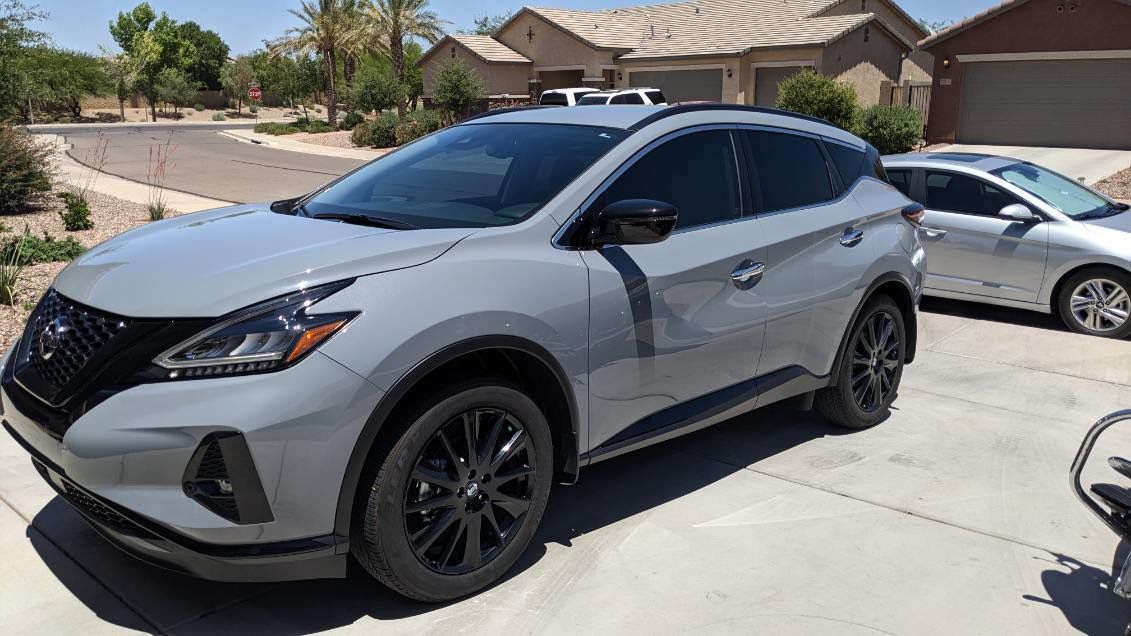 A silver nissan murano is parked in a driveway next to a silver car.