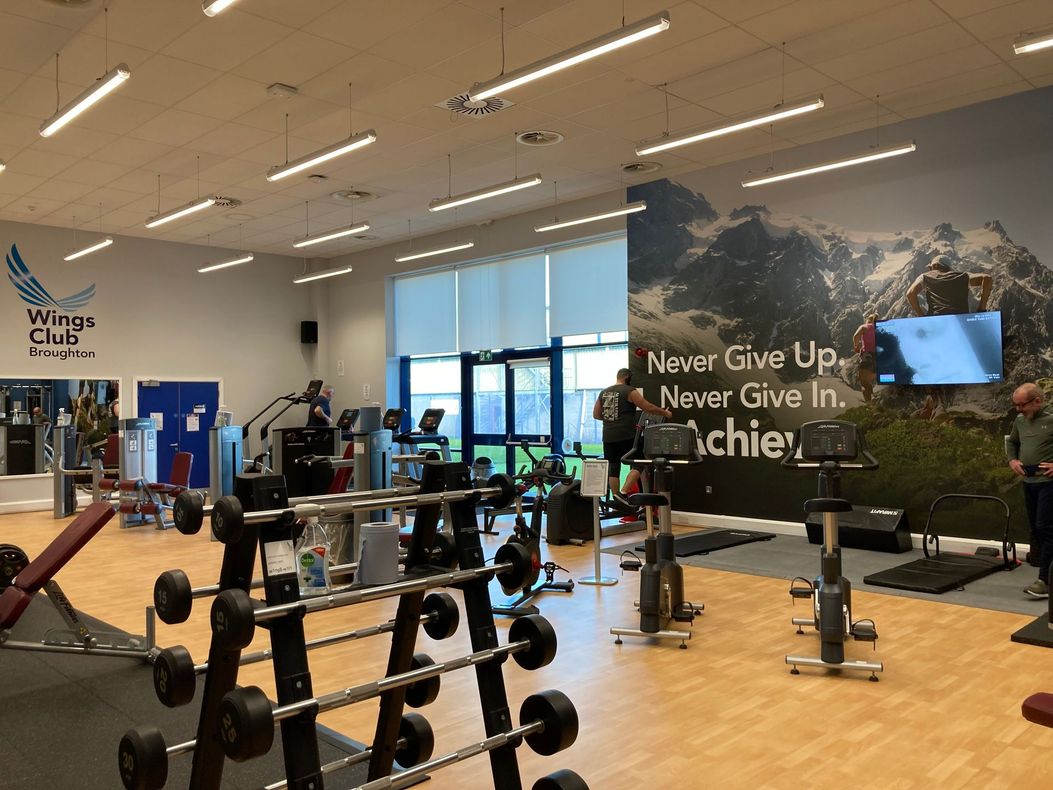 Gym interior with exercise equipment, including weights and stationary bikes; people exercising.
