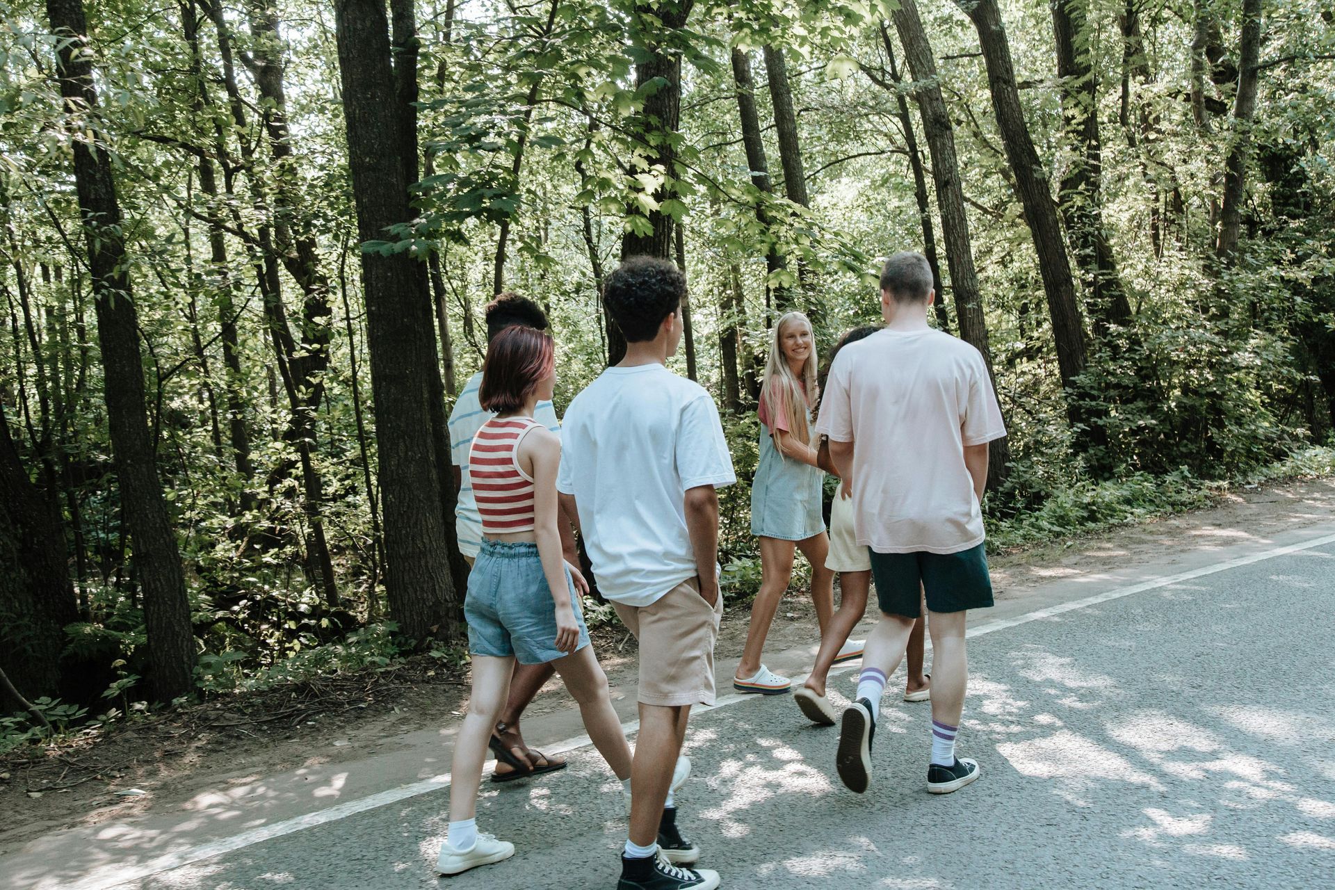 Group of friends walking on a road through a forest, talking and smiling.