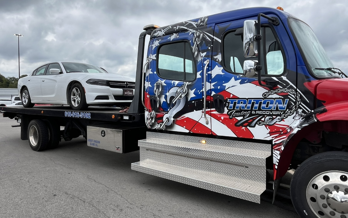 A white car being towed on a flatbed tow truck with an American flag design.