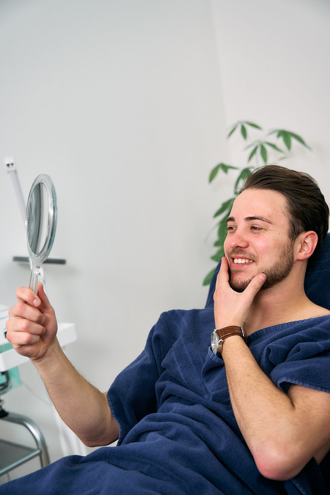 Eine Kosmetikerin sitzt neben einem zufriedenen Kunden der eine Gesichtsmaske auf der Haut hat und die Daumen hoch hält