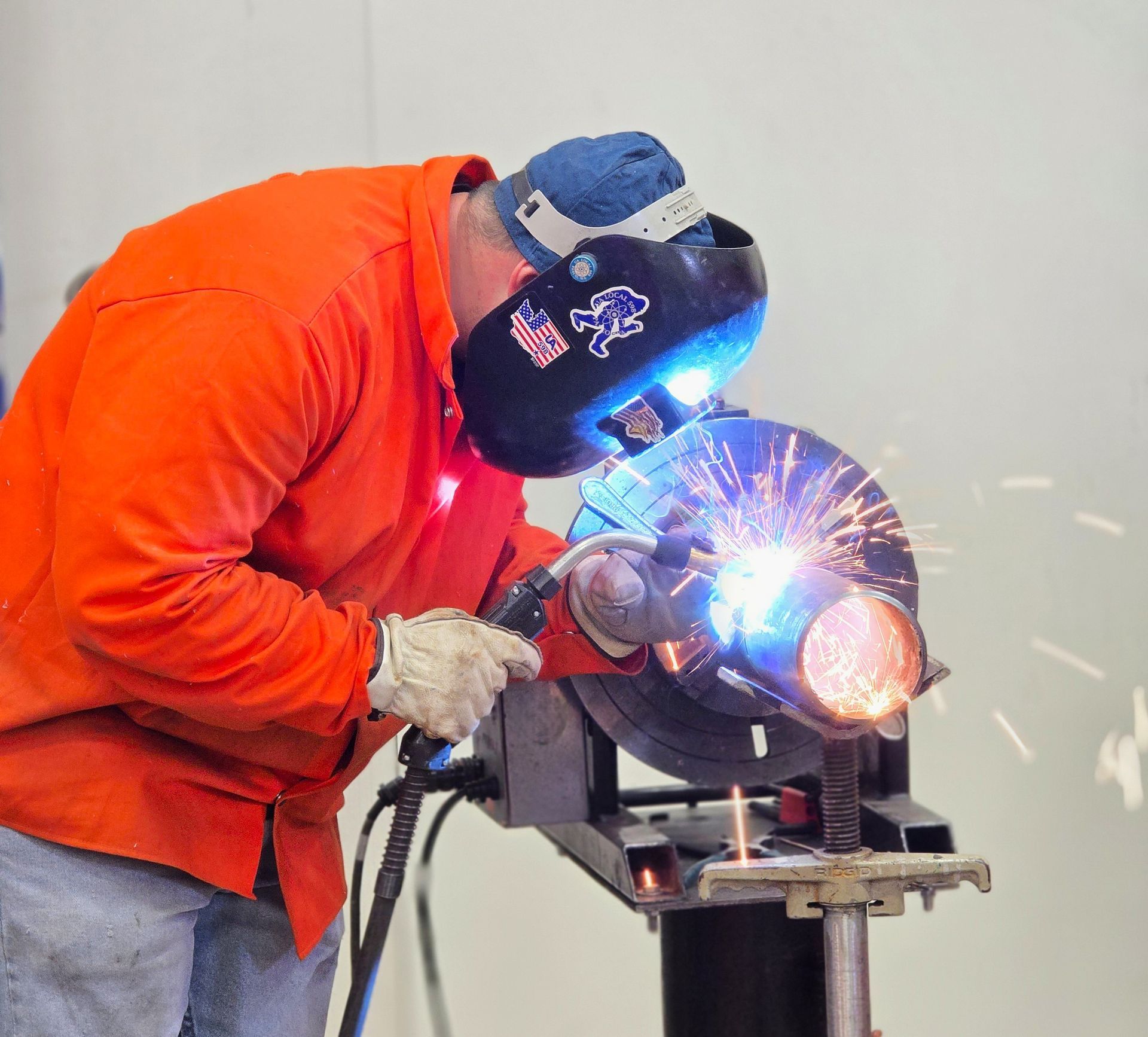 A man wearing a welding mask is welding a pipe