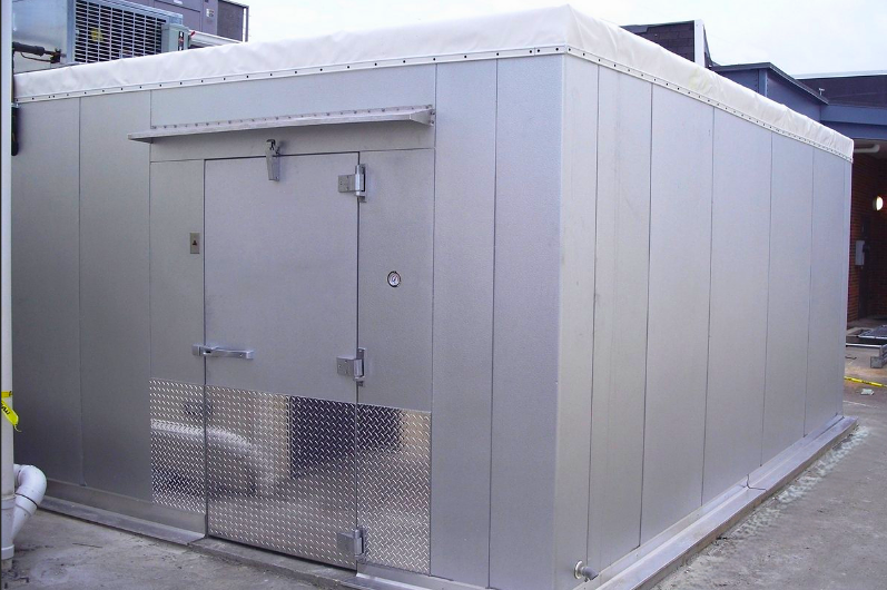 Walk-in freezer building with metal siding, white roof, and a closed stainless steel door.