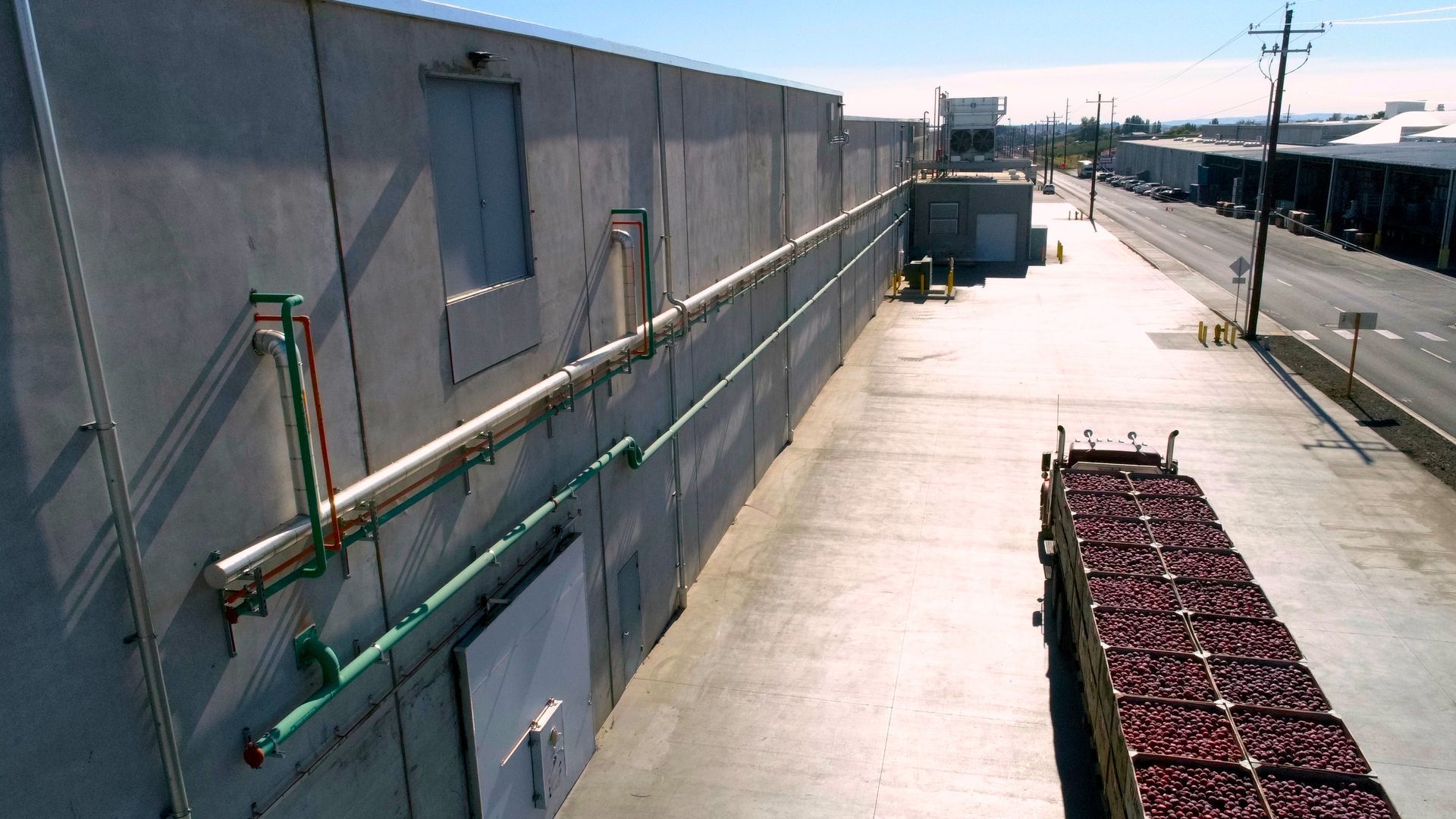 Truck loaded with red produce next to a concrete building on a sunny day.