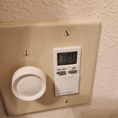 A thermostat is sitting on a wall next to a light switch.