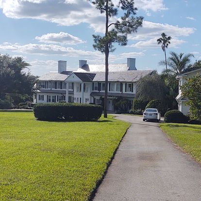 A white car is parked in front of a large white house.