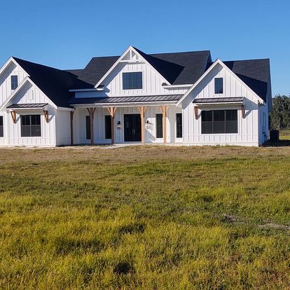 A large white house with a black roof is sitting in the middle of a grassy field.