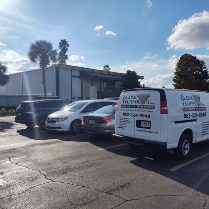 A row of cars are parked in a parking lot in front of a building.