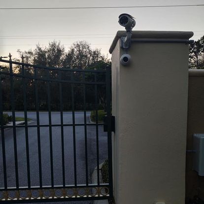 A security camera is mounted on top of a fence.