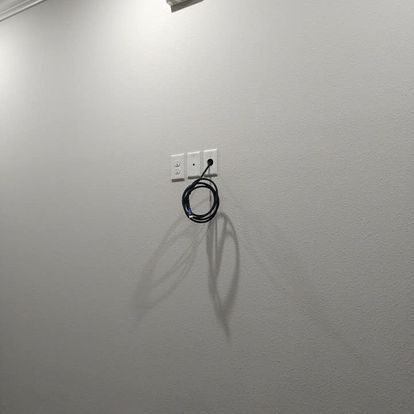 A cable is hanging from a hook on a white wall.