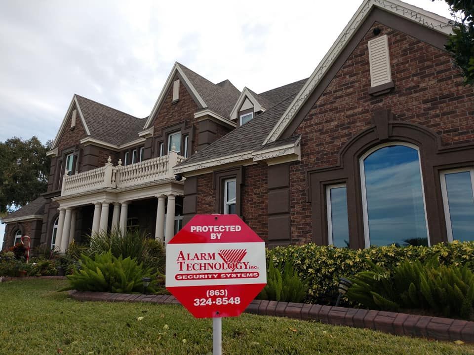 A large brick house with a red alarm technology sign in front of it.