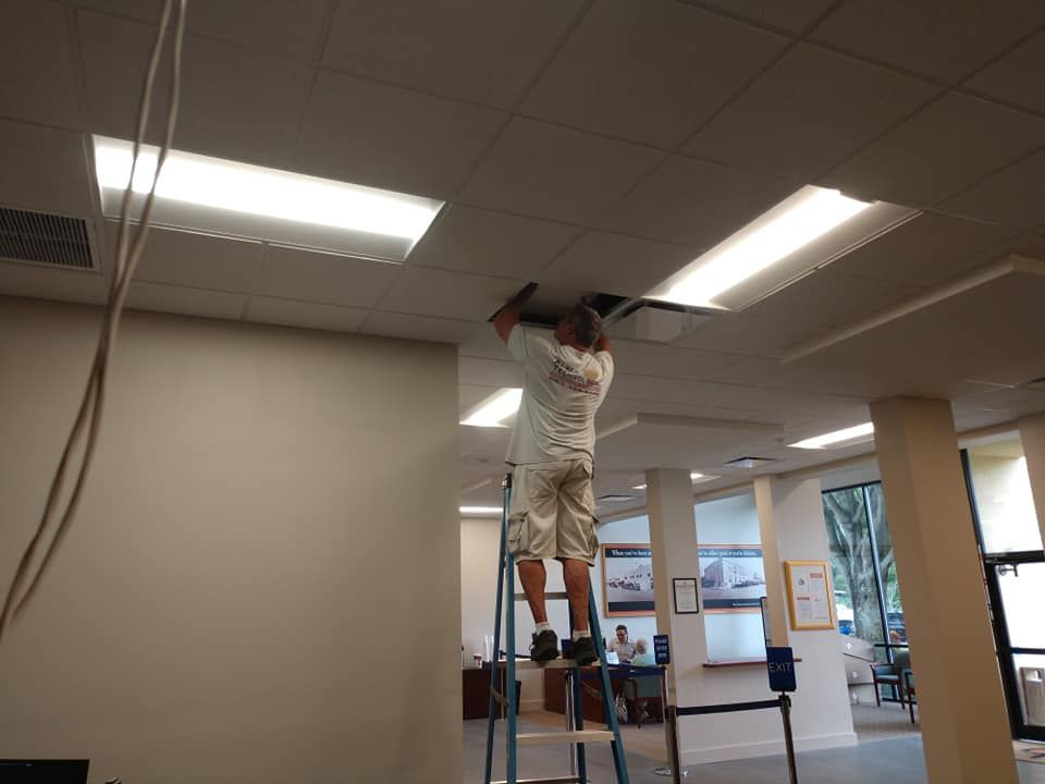 A man is standing on a ladder working on a ceiling light.