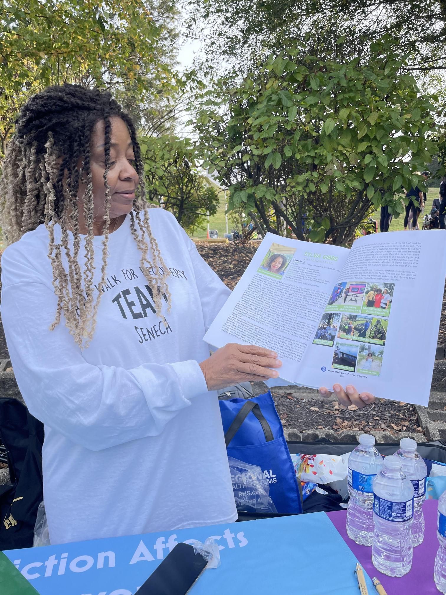 A woman is holding a piece of paper in front of a table with water bottles.