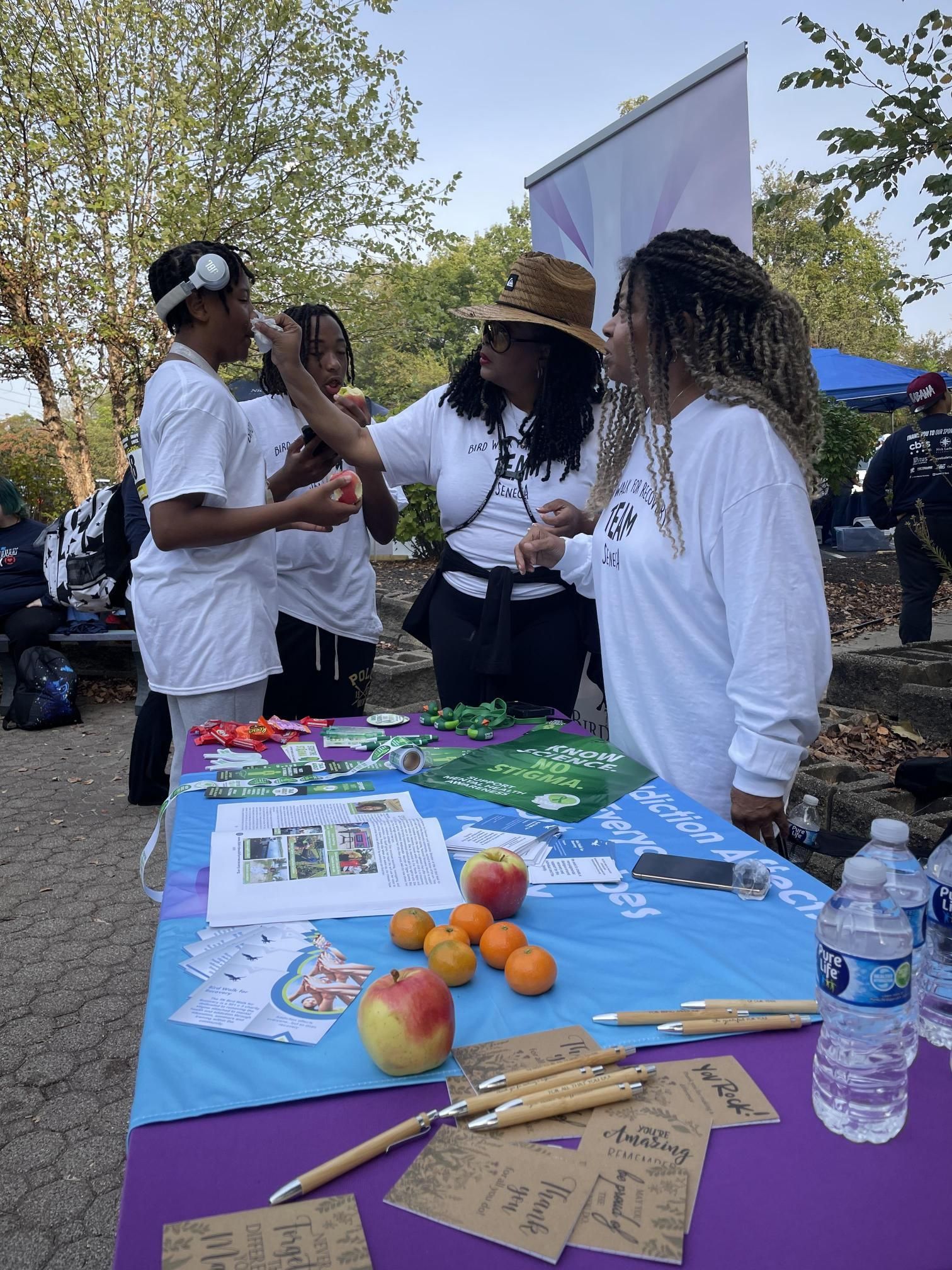 A group of people are standing around a table with fruit and water bottles.