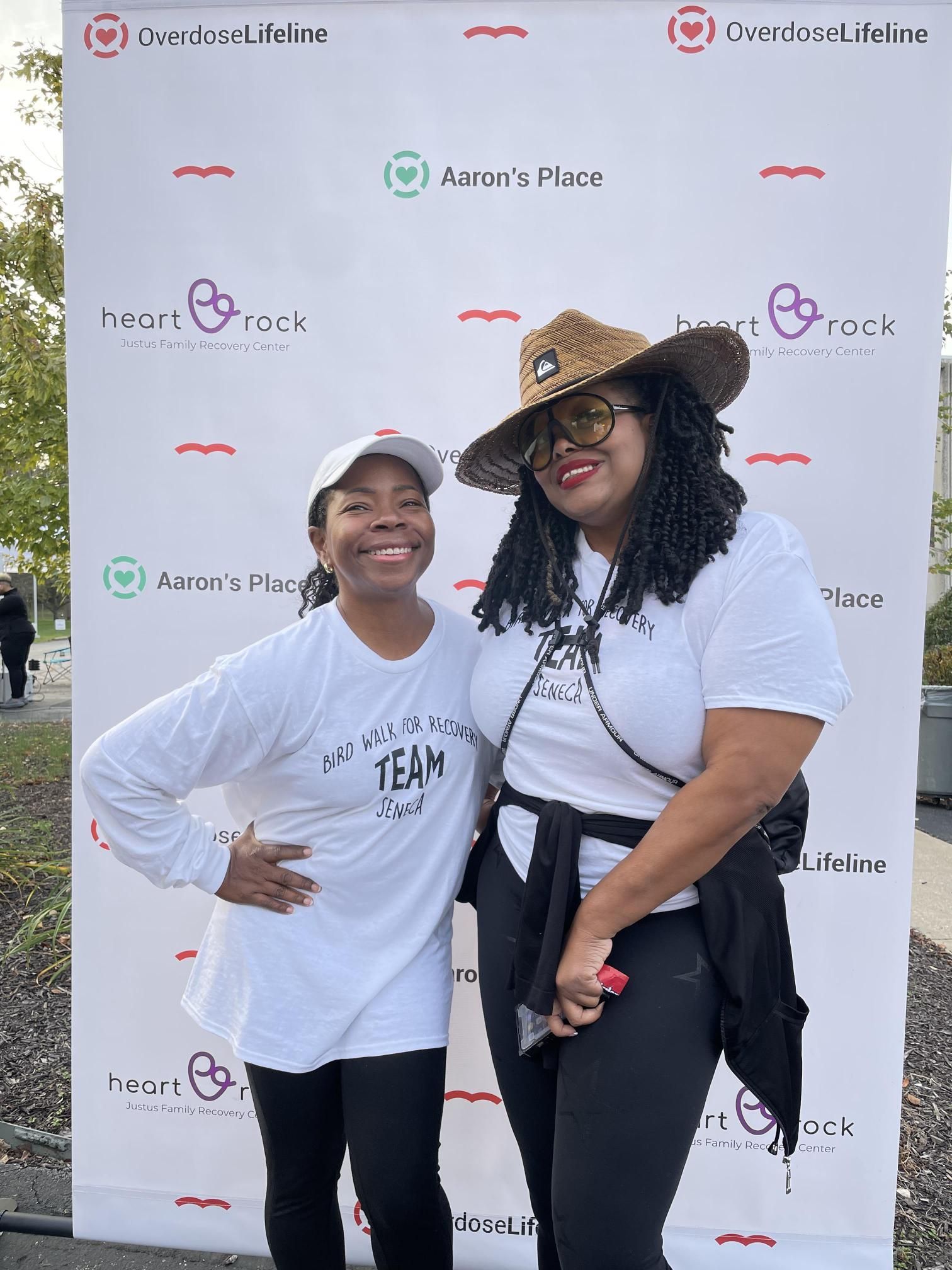 Two women are posing for a picture in front of a wall.
