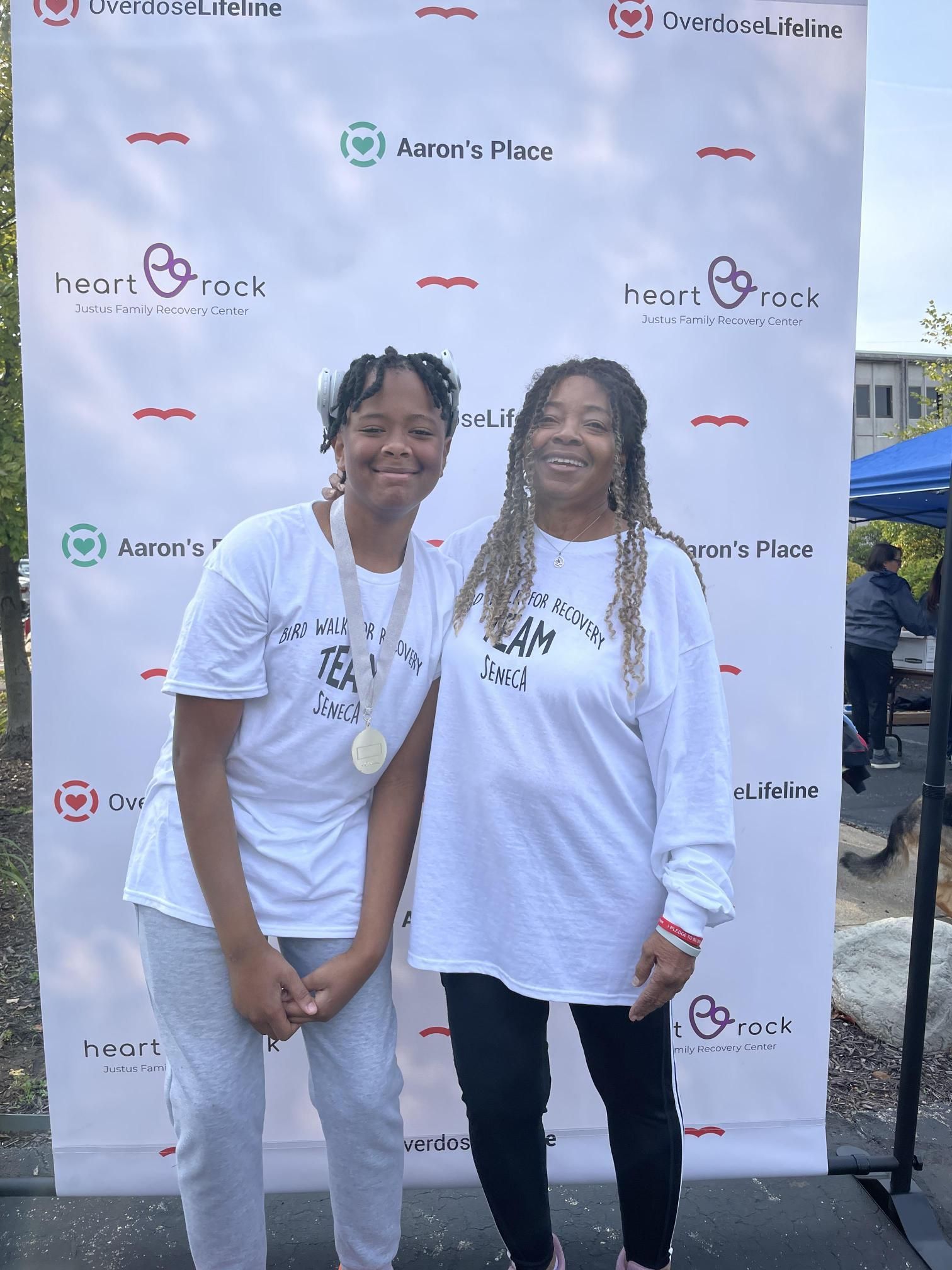 Two women are posing for a picture in front of a wall that says heart rock