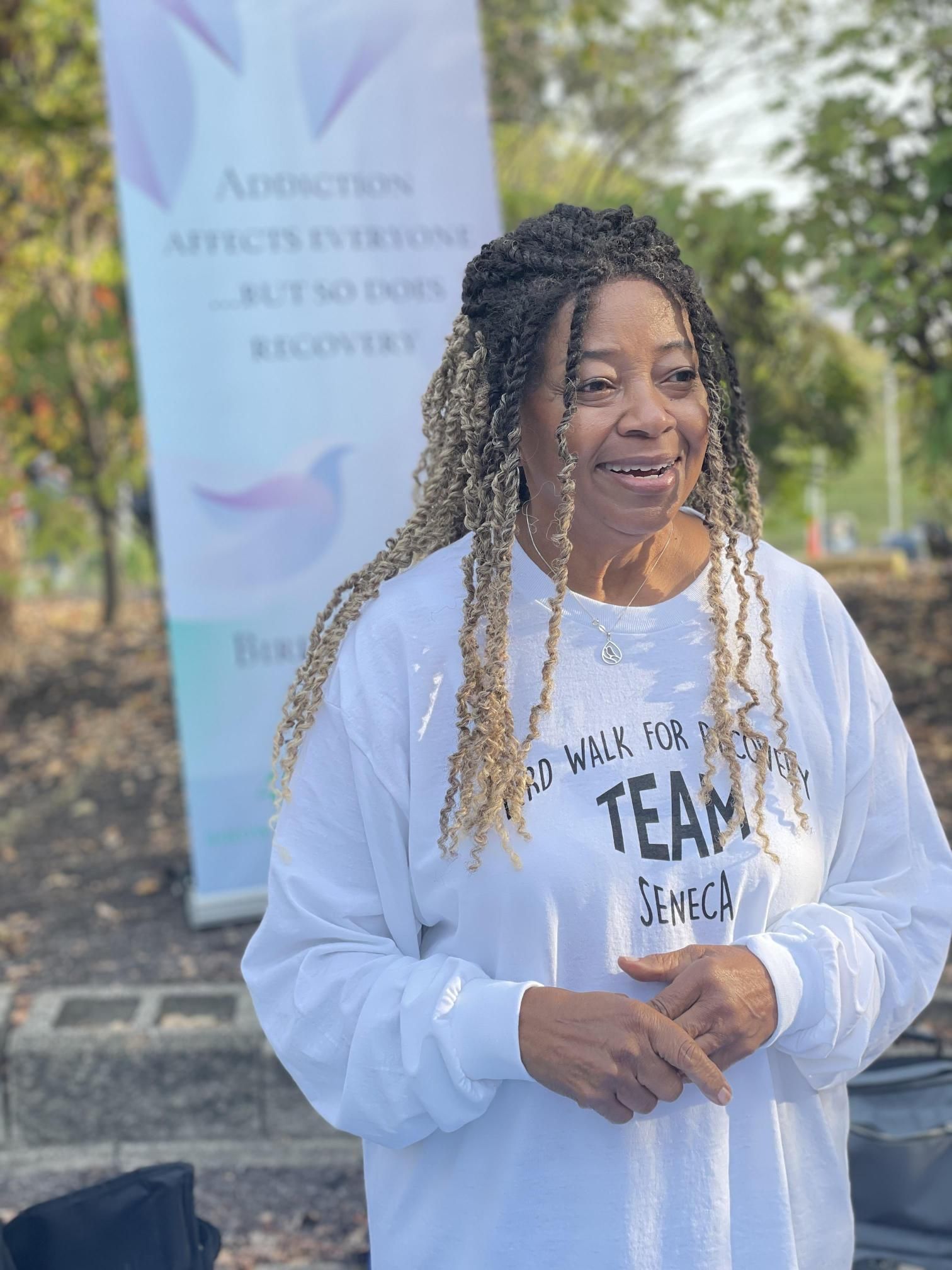 A woman wearing a white sweatshirt with the word team on it is standing in front of a sign.