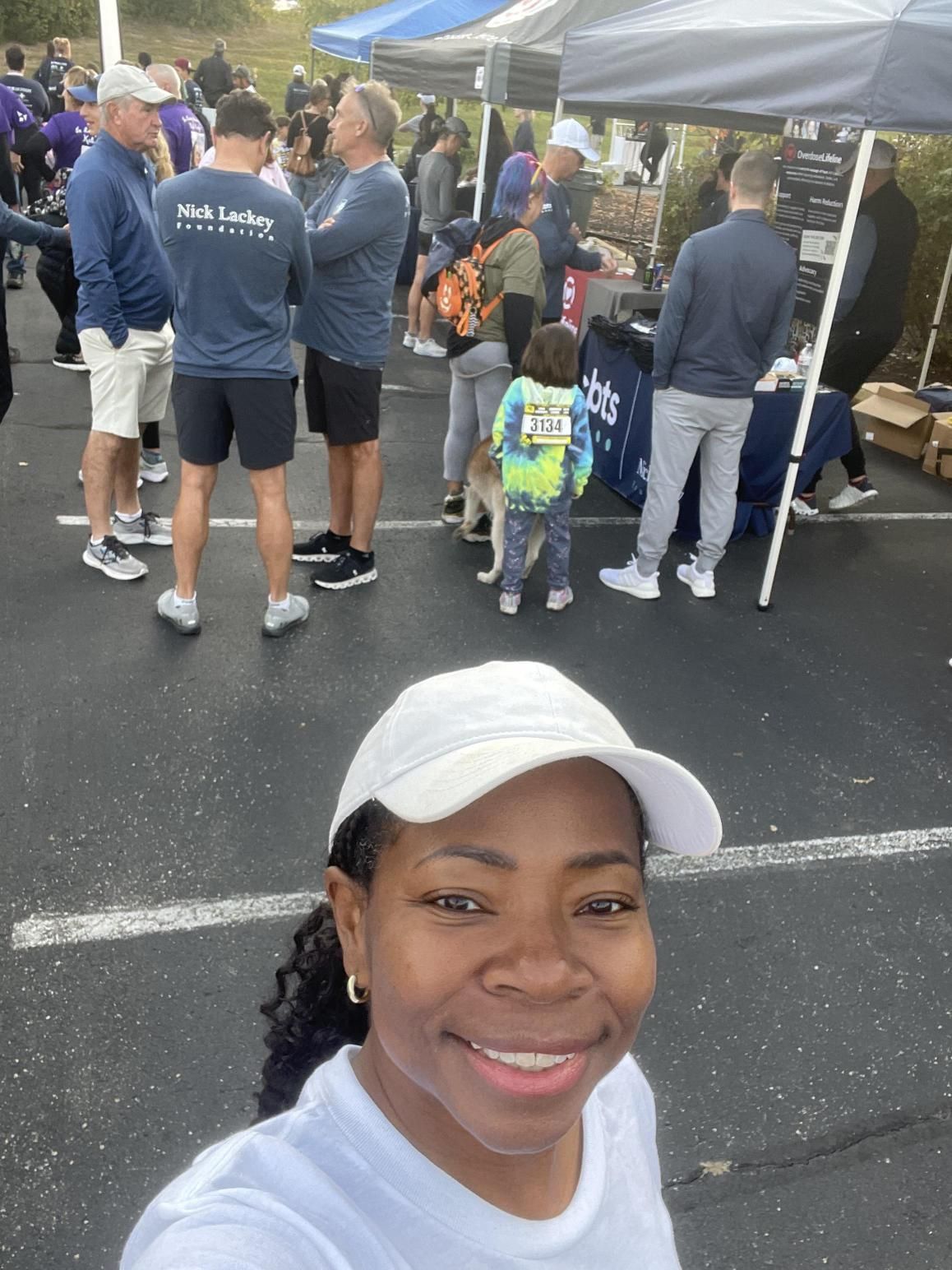 A woman in a white hat is smiling in front of a crowd of people