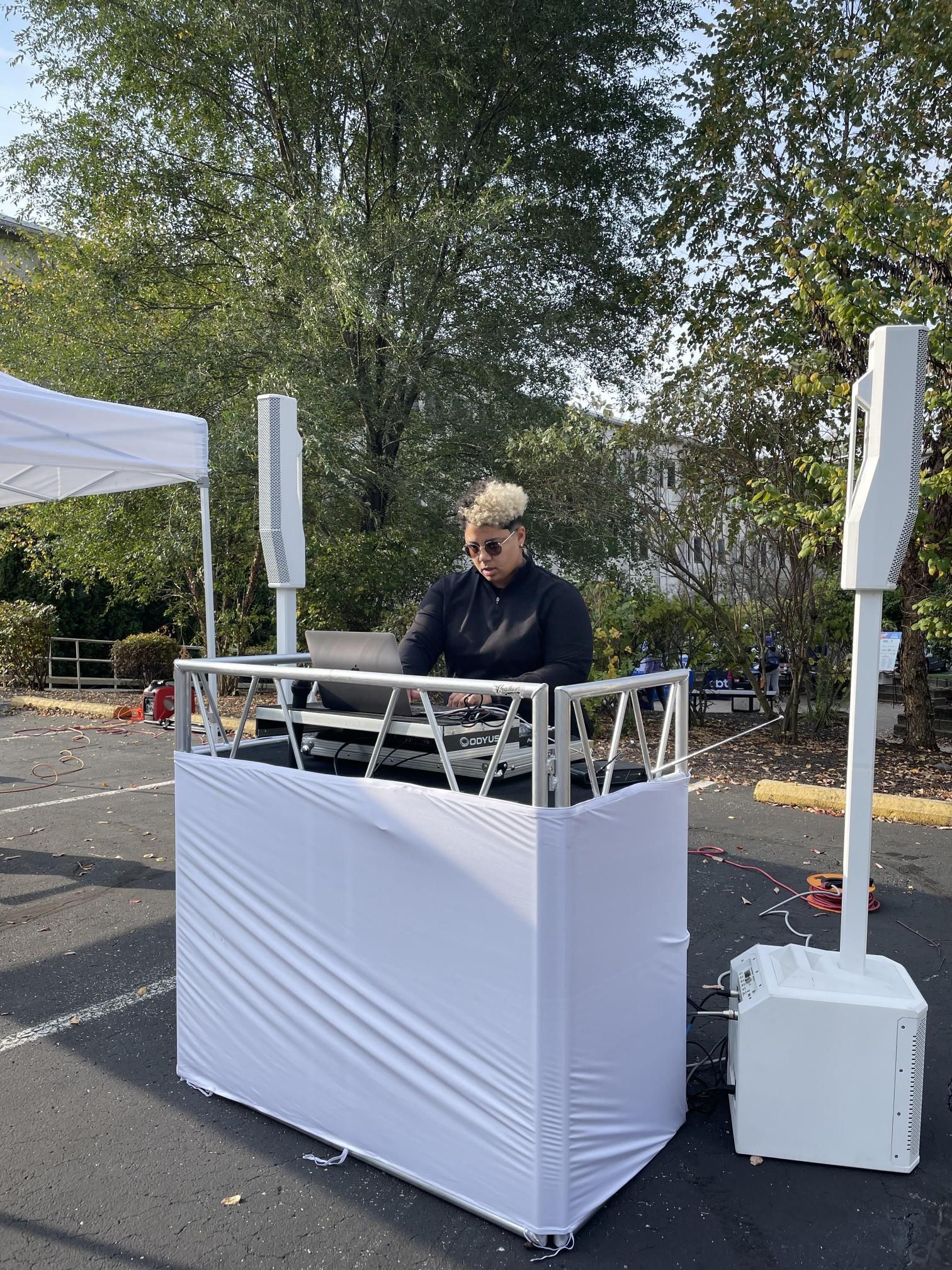 A man is playing music at a dj booth in a parking lot.