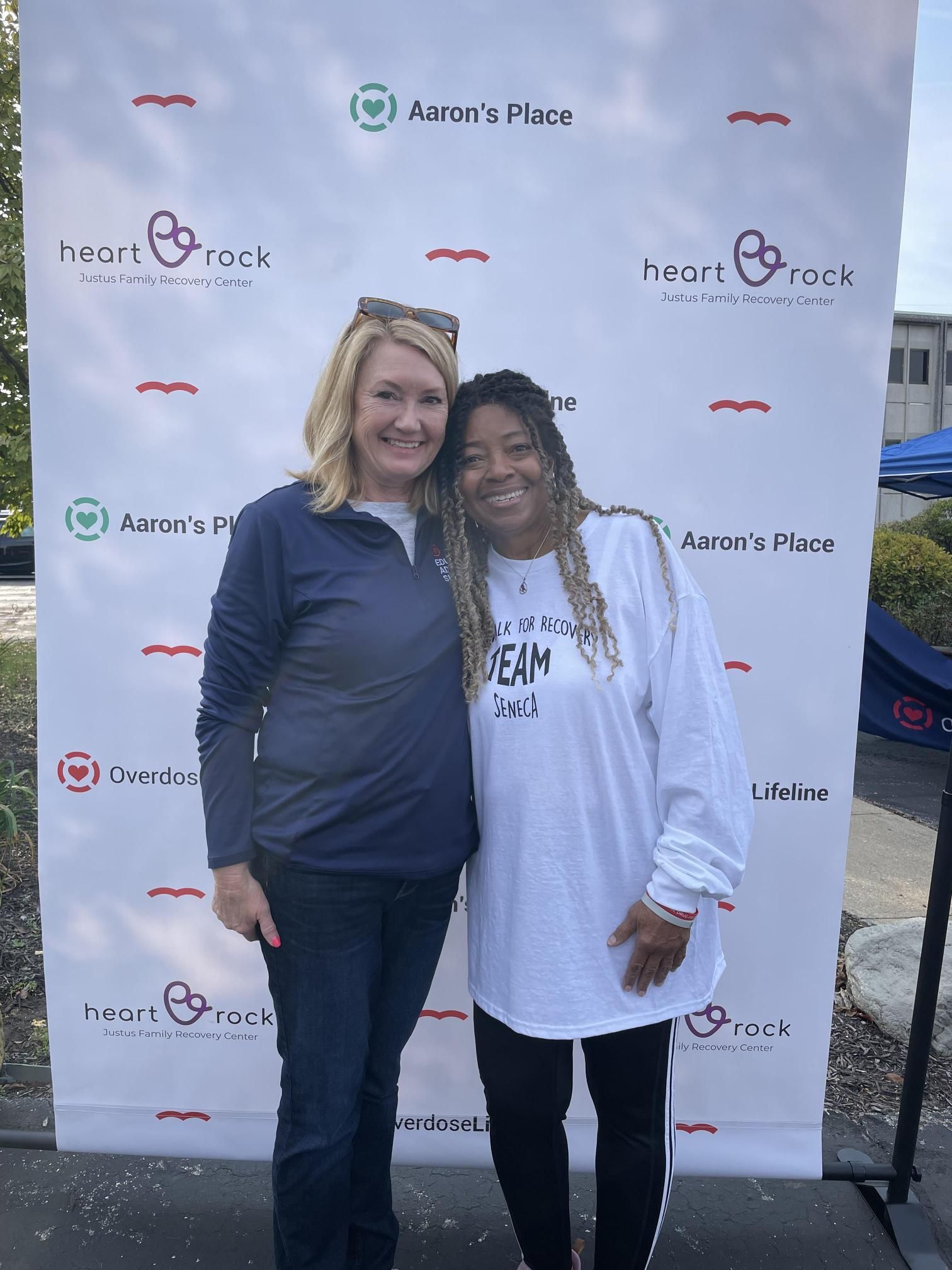 Two women are posing for a picture in front of a backdrop.