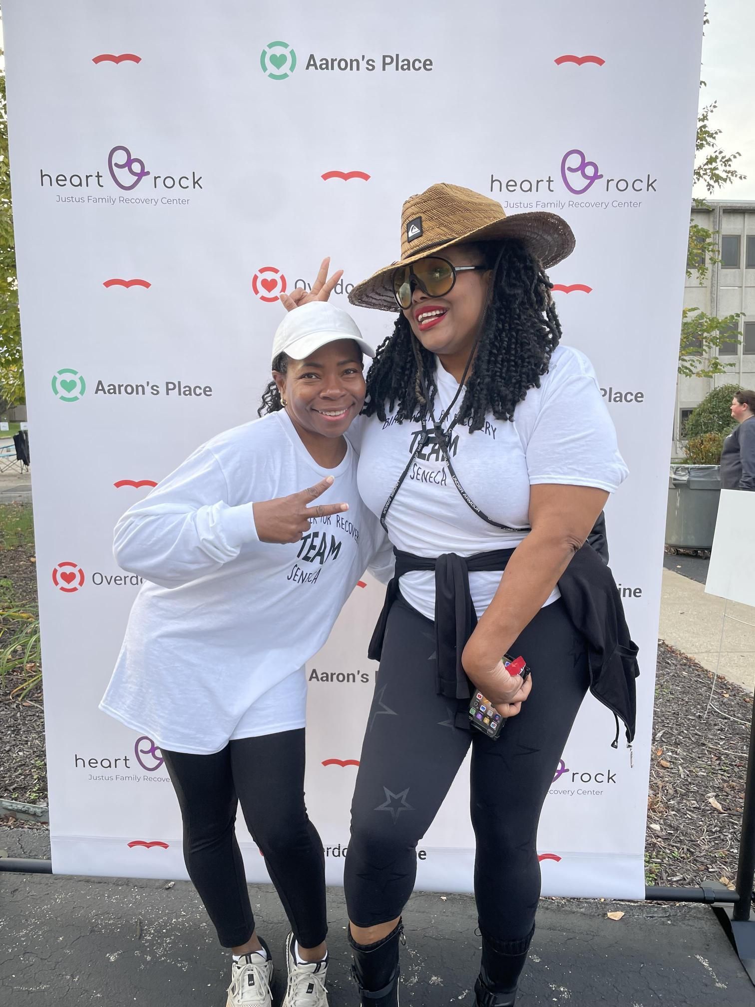 Two women are posing for a picture in front of a white backdrop.
