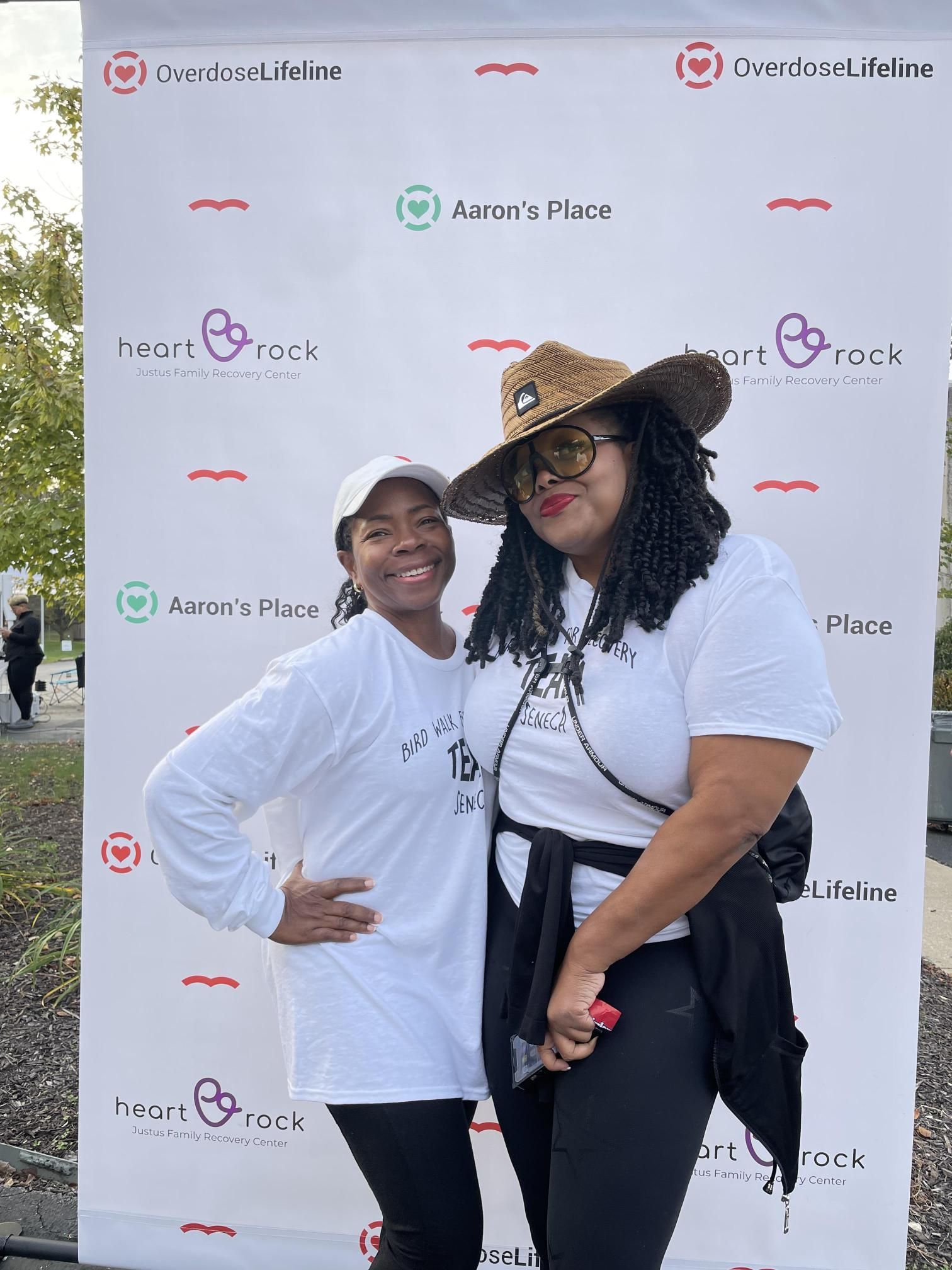Two women are posing for a picture in front of a white backdrop.