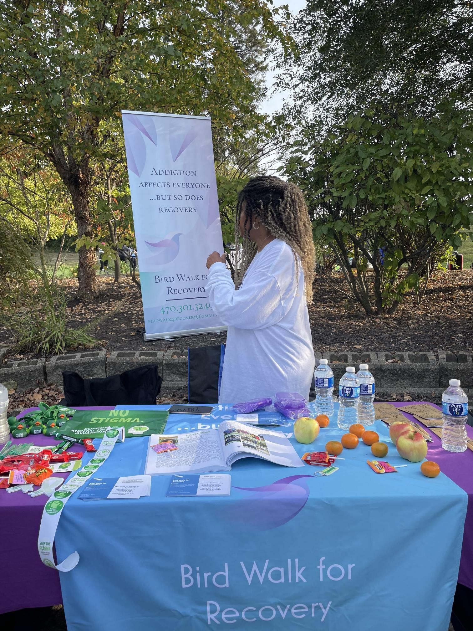 A woman is standing at a table with a sign that says bird walk for recovery.