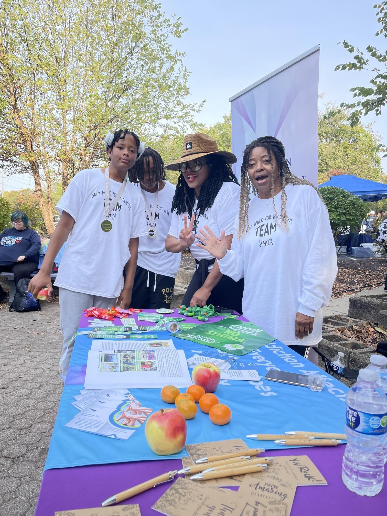 A group of people are standing around a table with fruit on it.