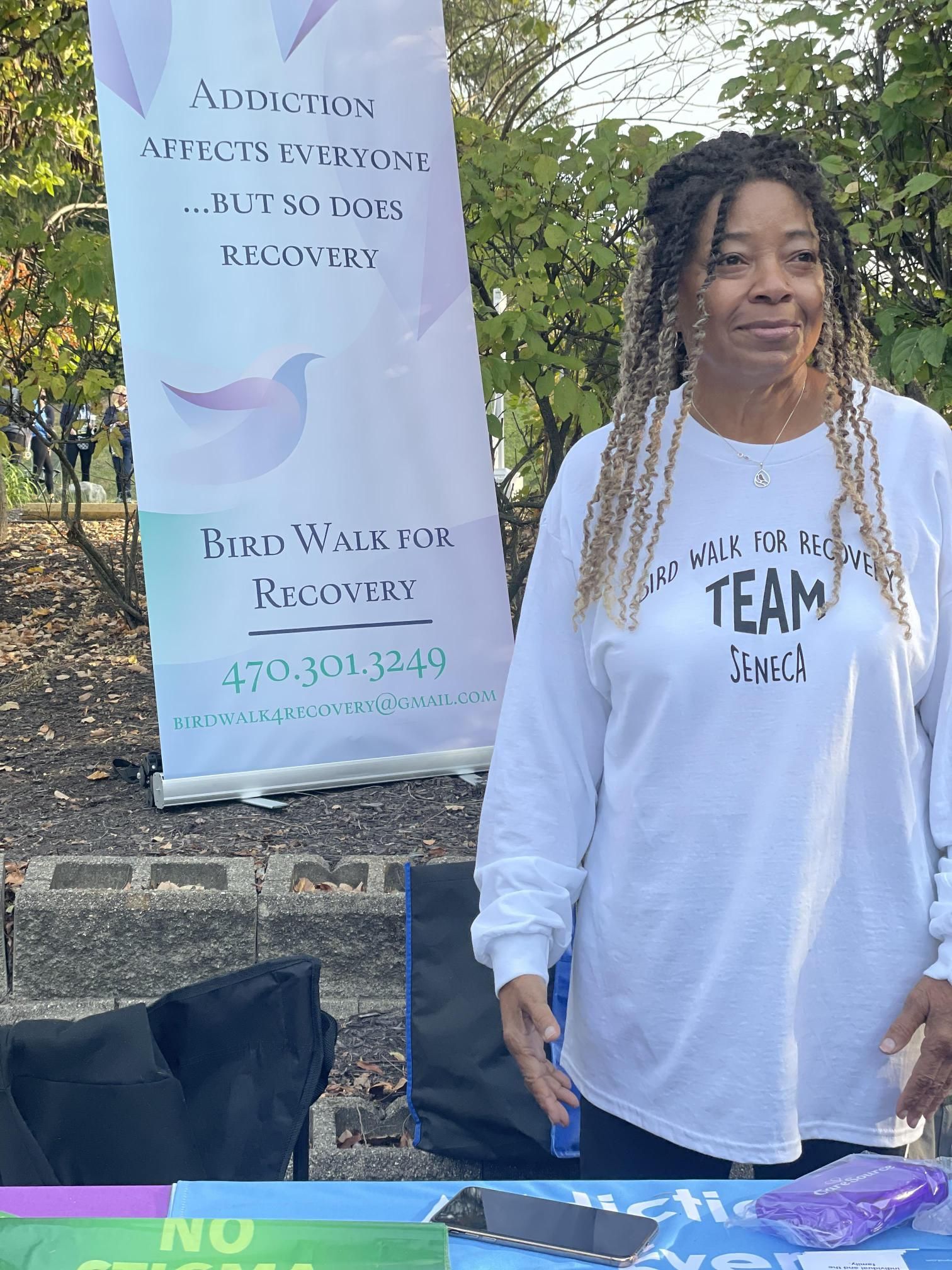 A woman in a white shirt is standing in front of a sign.