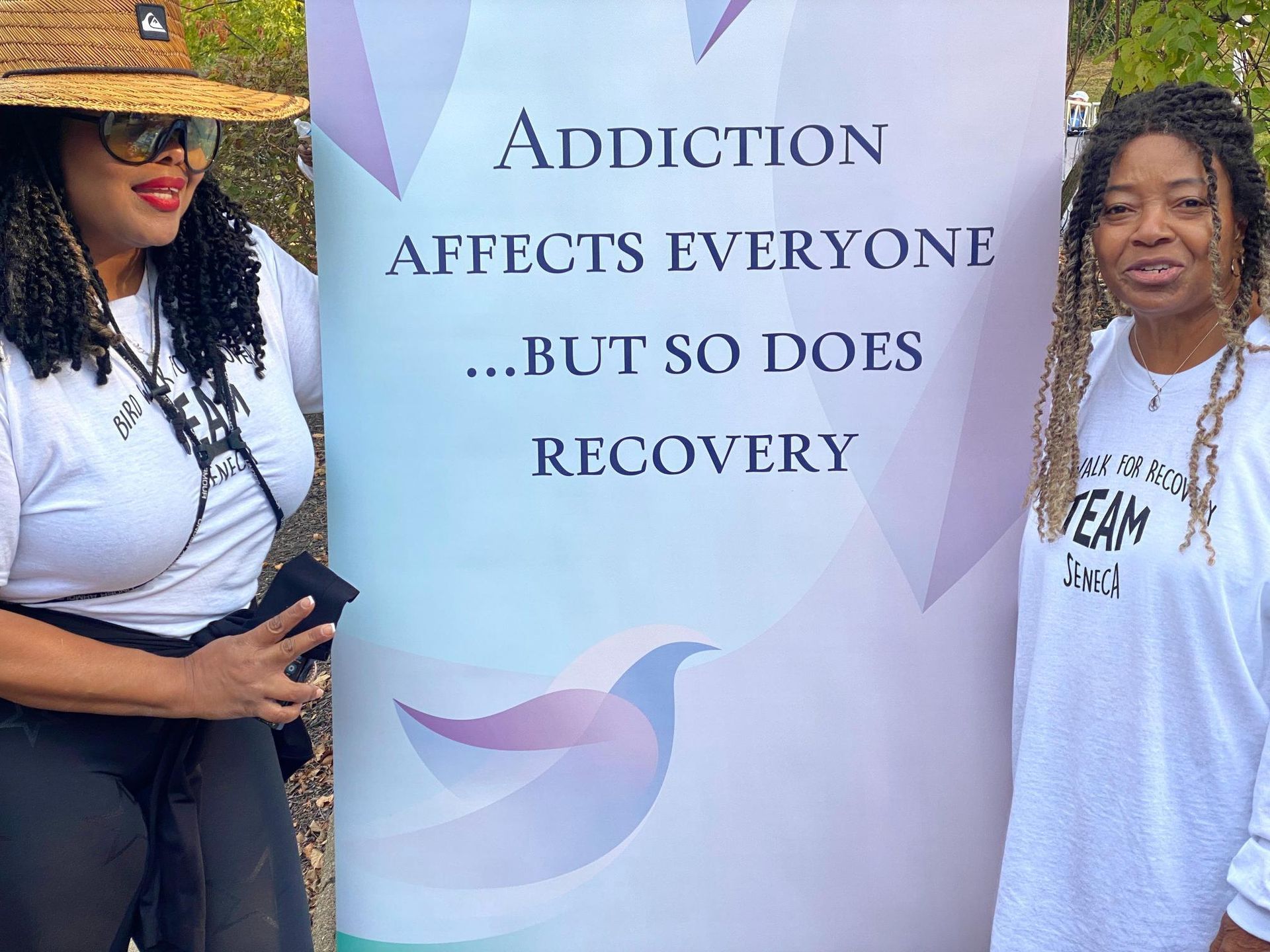 Two women standing next to a sign that says addiction affects everyone but so does recovery