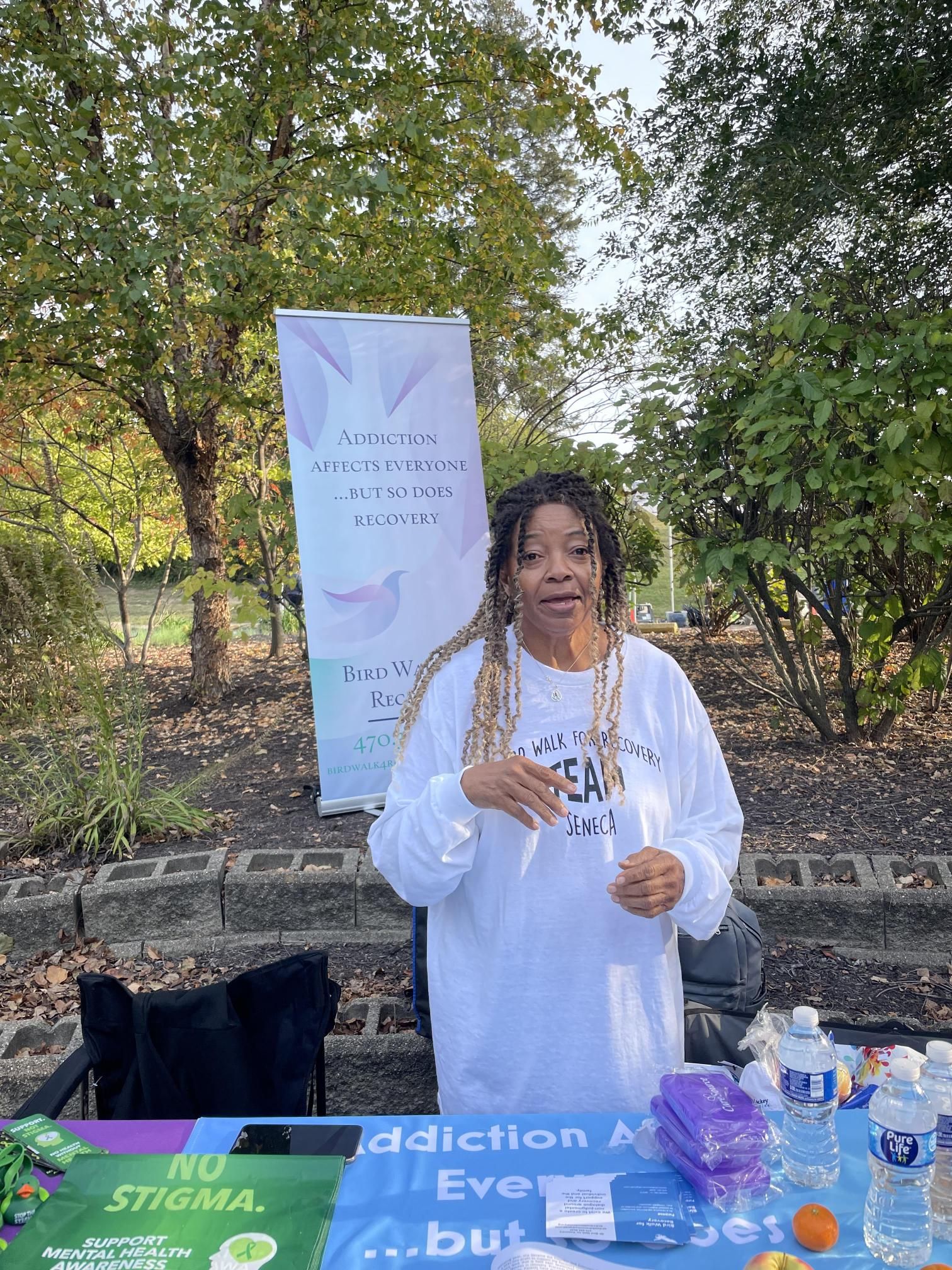 A woman is standing in front of a table with a sign on it.