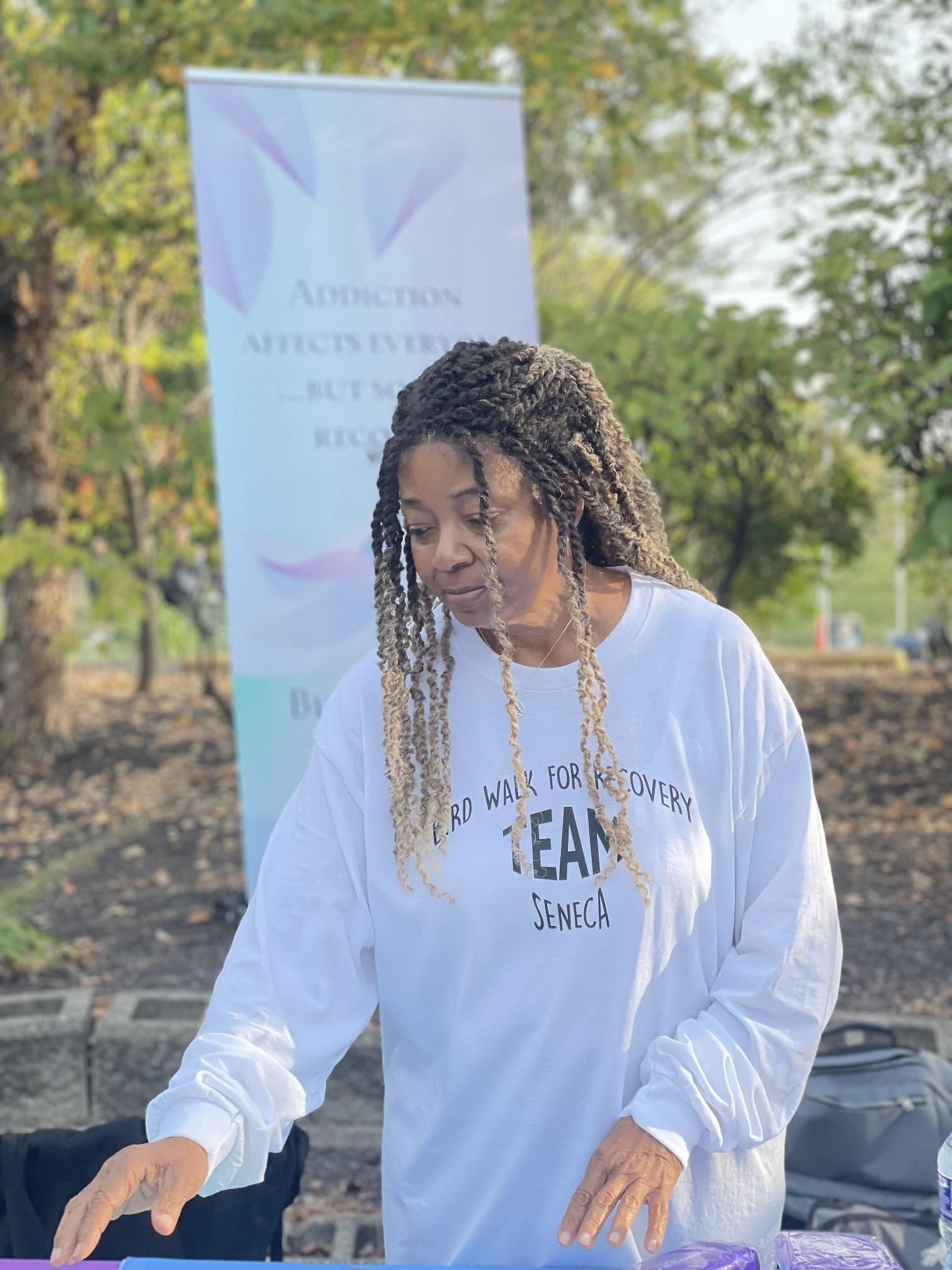 A woman in a white shirt is standing in front of a sign.