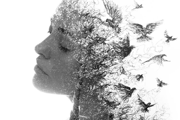 A double exposure of a woman 's face with birds flying out of it.