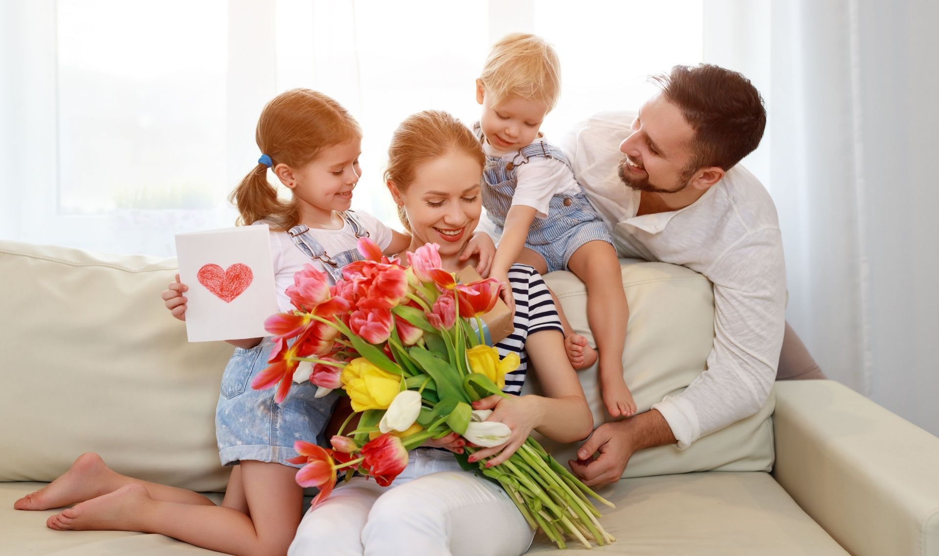 A family is sitting on a couch holding flowers and a card.