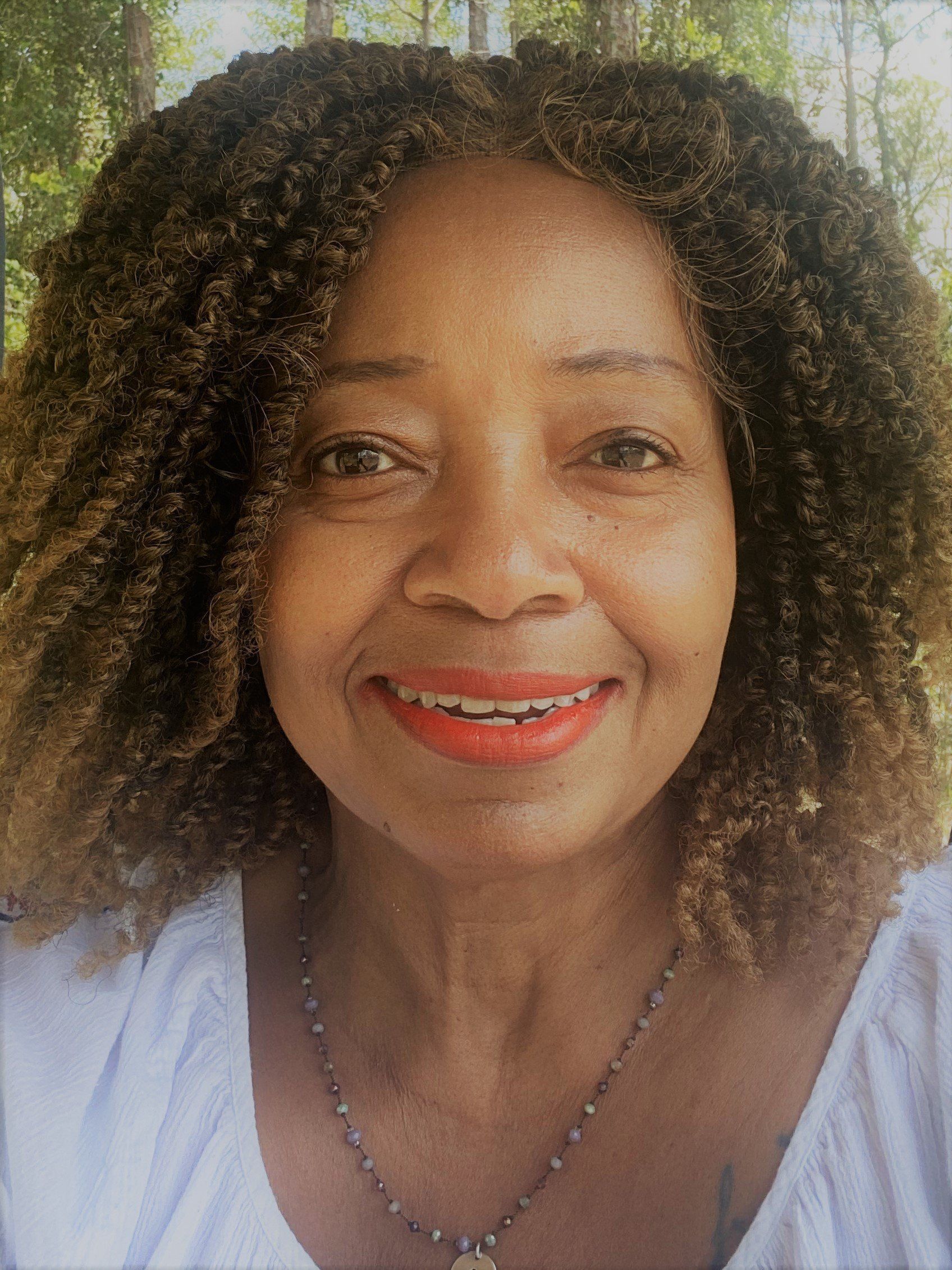 A woman with curly hair and red lipstick is smiling for the camera.