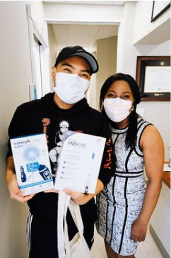 A man and a woman wearing face masks are holding a box of waterpik products.