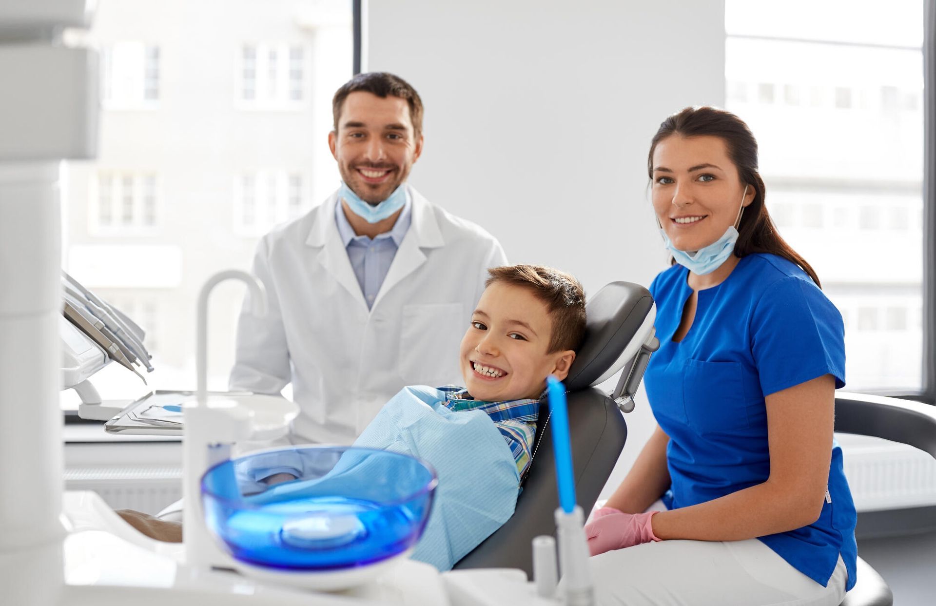 Dentist, assistant, and smiling child at dental office. The child is in a chair.