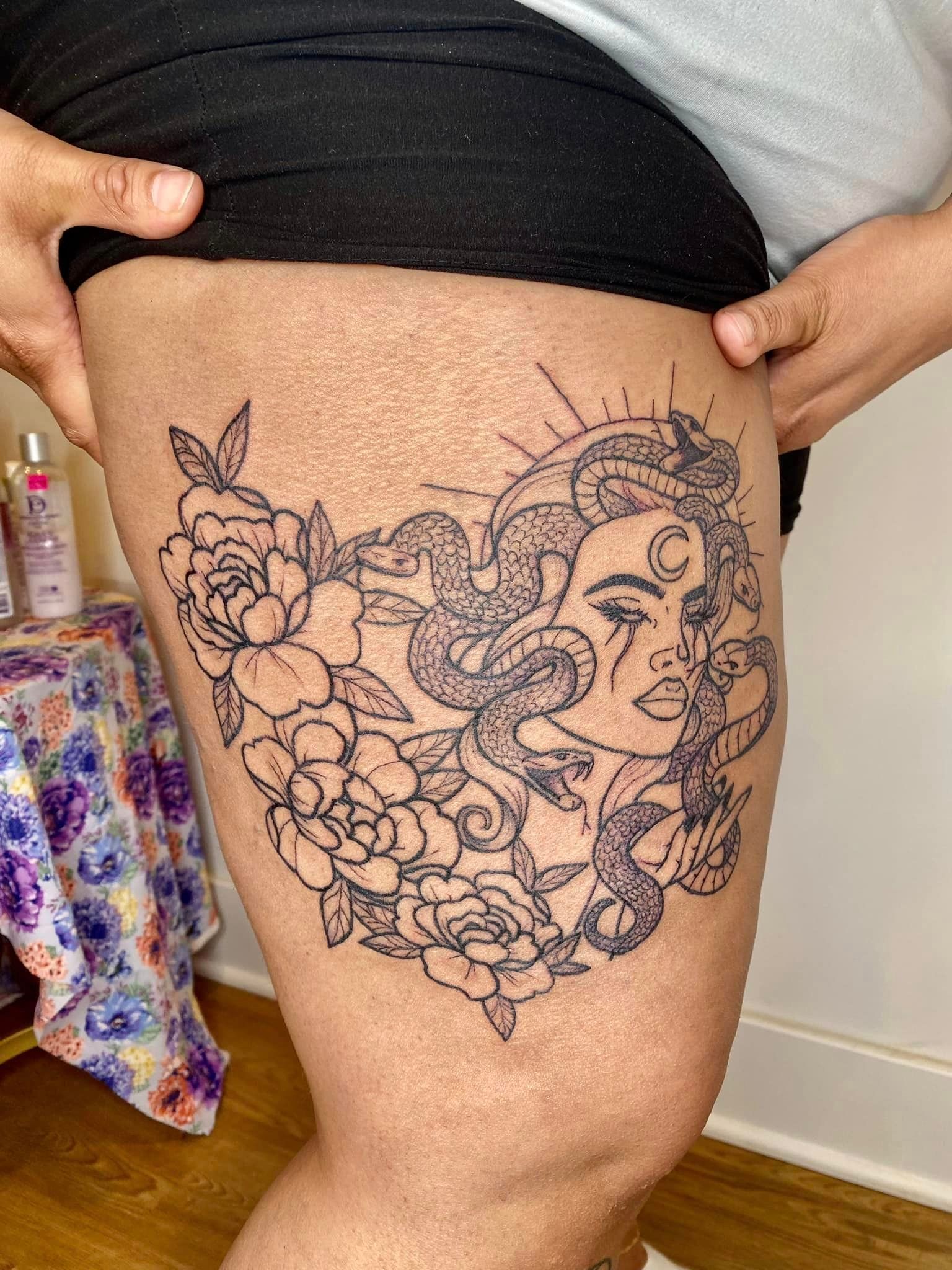 A woman has a tattoo of a woman surrounded by flowers on her thigh.