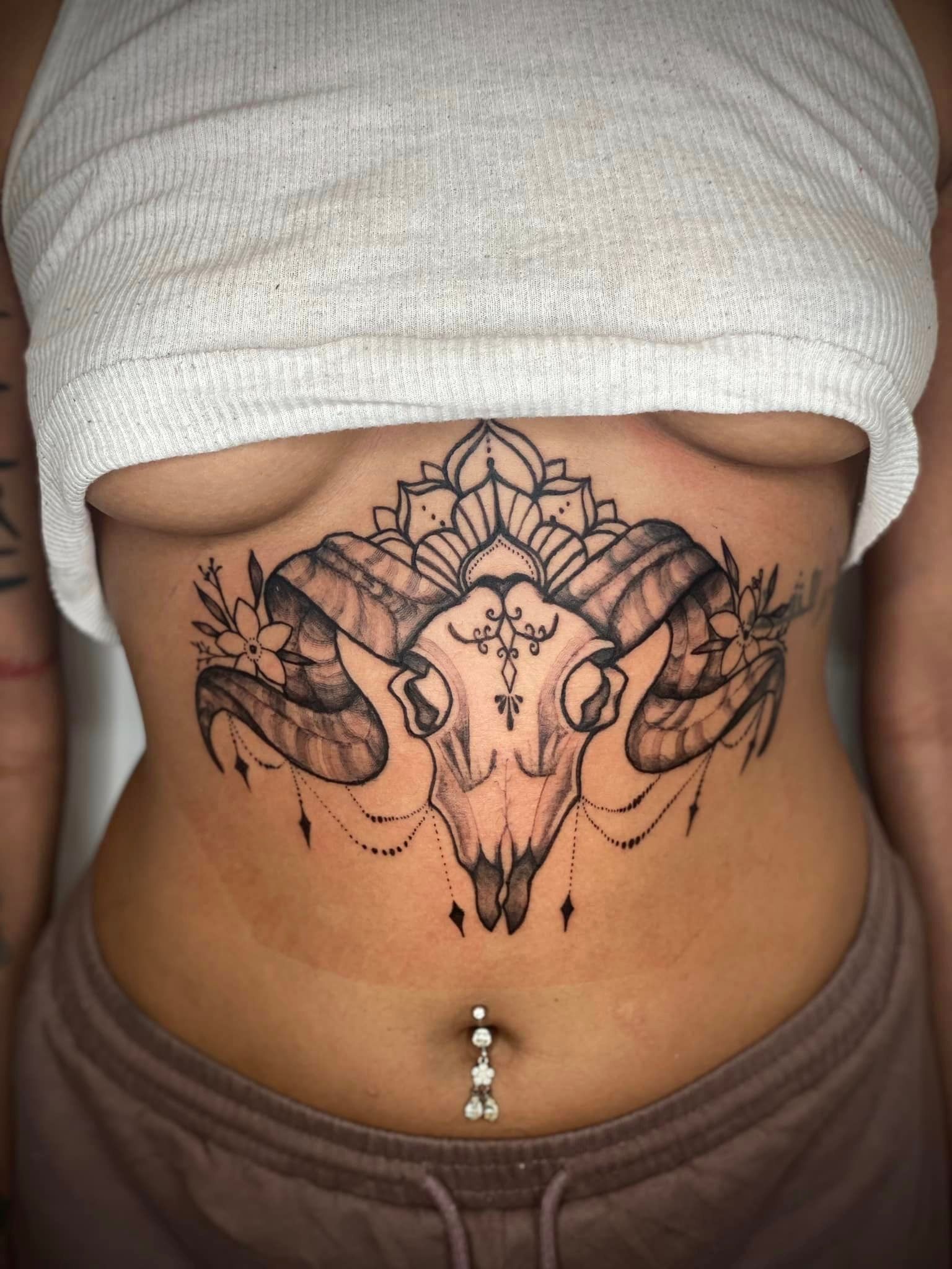 A woman has a tattoo of a ram skull on her stomach.