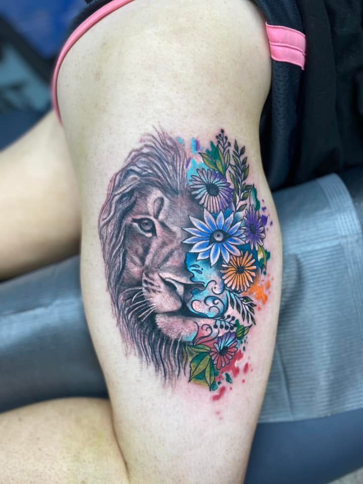 A woman has a tattoo of a lion and flowers on her thigh.