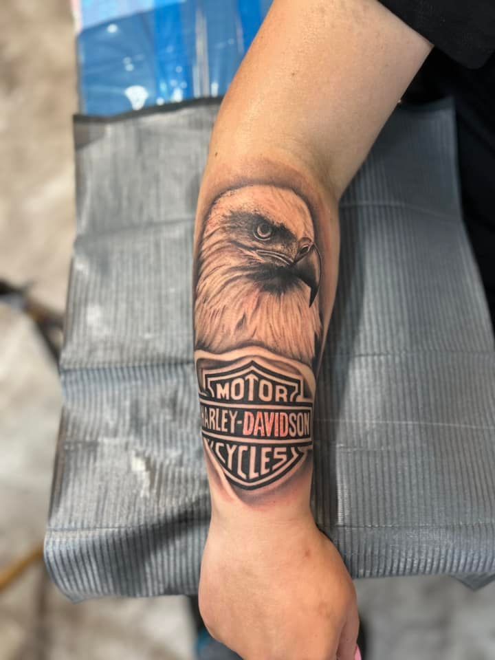 A woman has a harley davidson tattoo on her forearm.